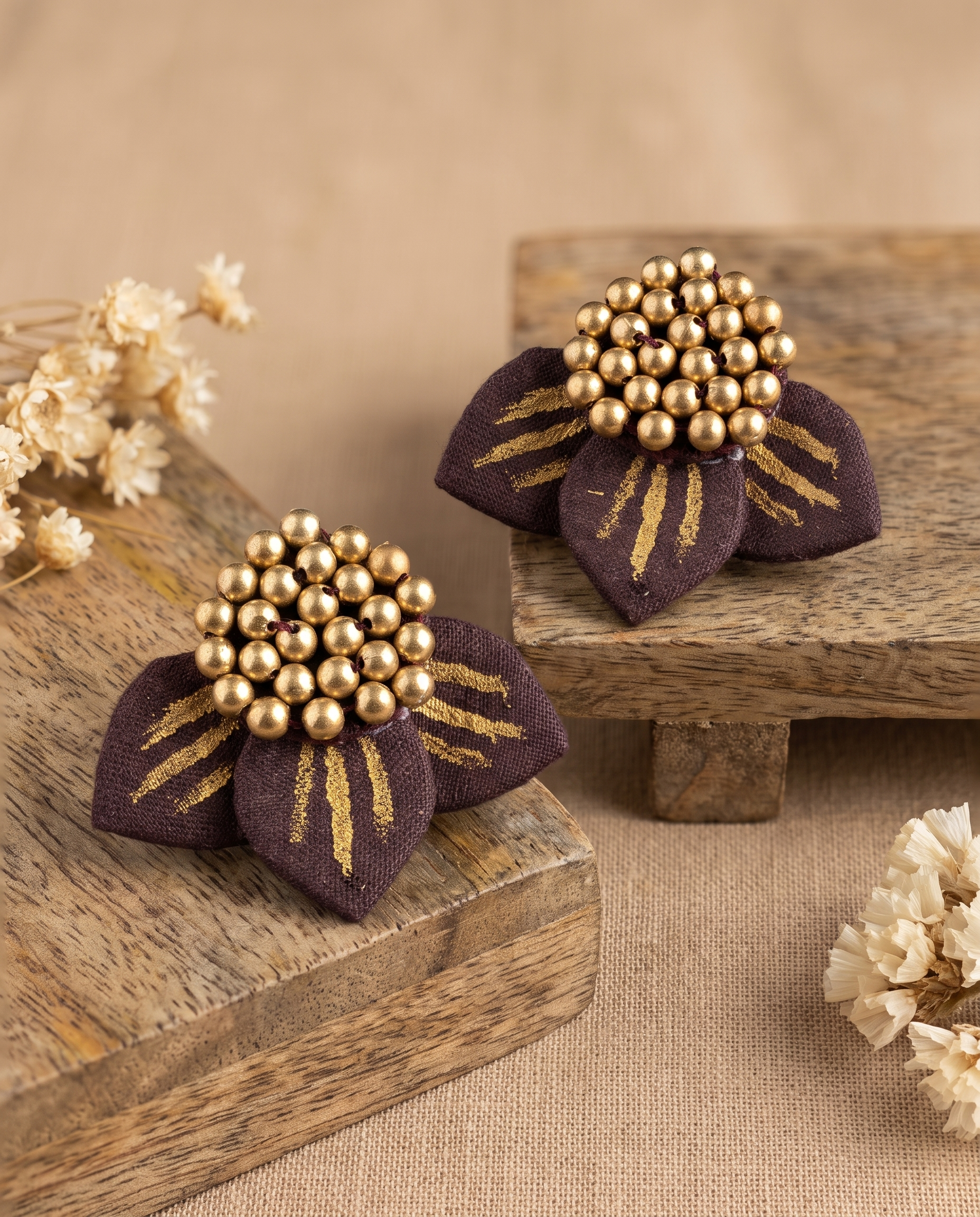 Maroon fabric floral stud earrings styled on wooden risers with dried flowers