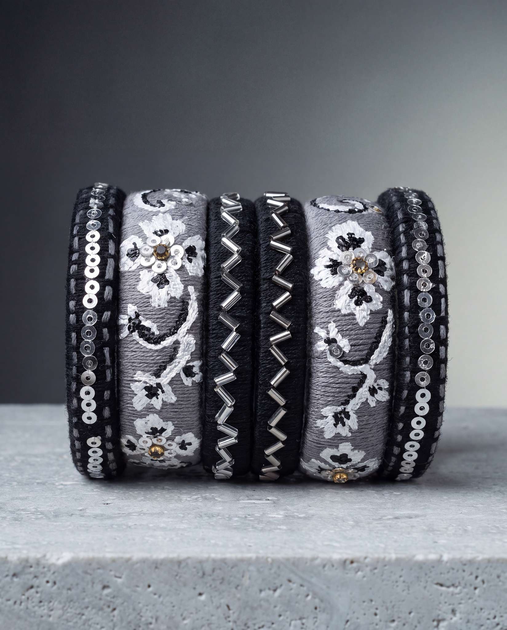 Black and grey silk thread bangles with silver beadwork on dramatic gray gradient background