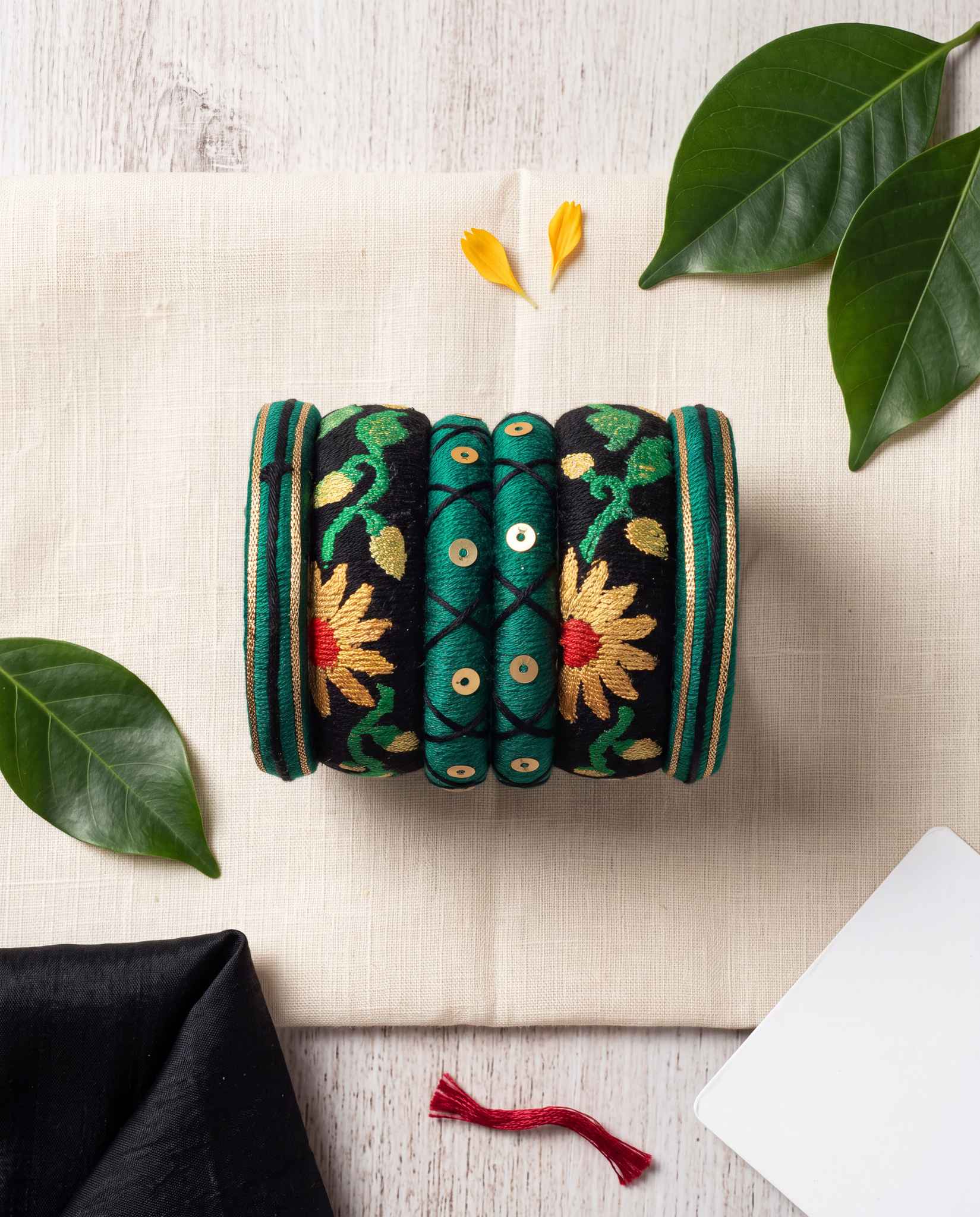 Green and black sunflower silk thread bangle set styled with leaves on a fabric backdrop