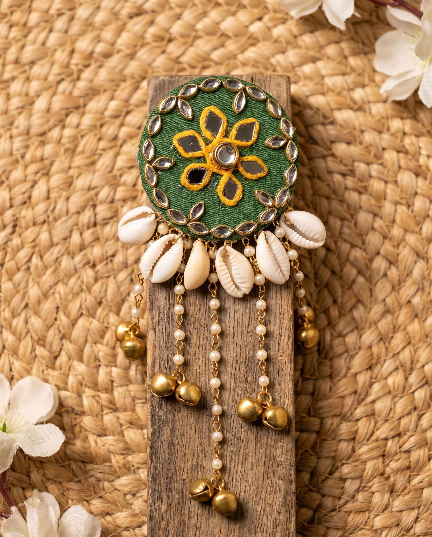 Top-down view of green mirror hair brooch with cowrie shell fringe on wood block