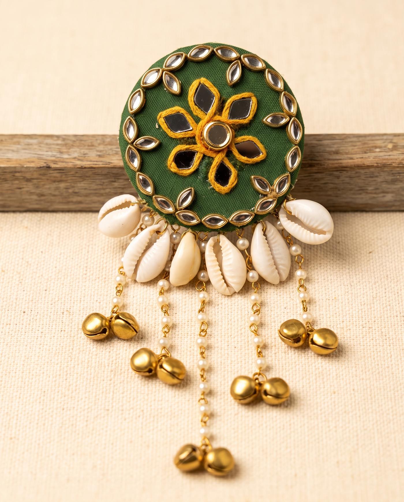 Green mirror work hair brooch with cowrie shells and gold bell tassels on beige linen