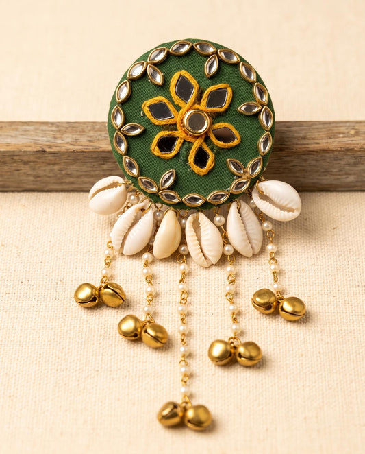 Green mirror work hair brooch with cowrie shells and gold bell tassels on beige linen