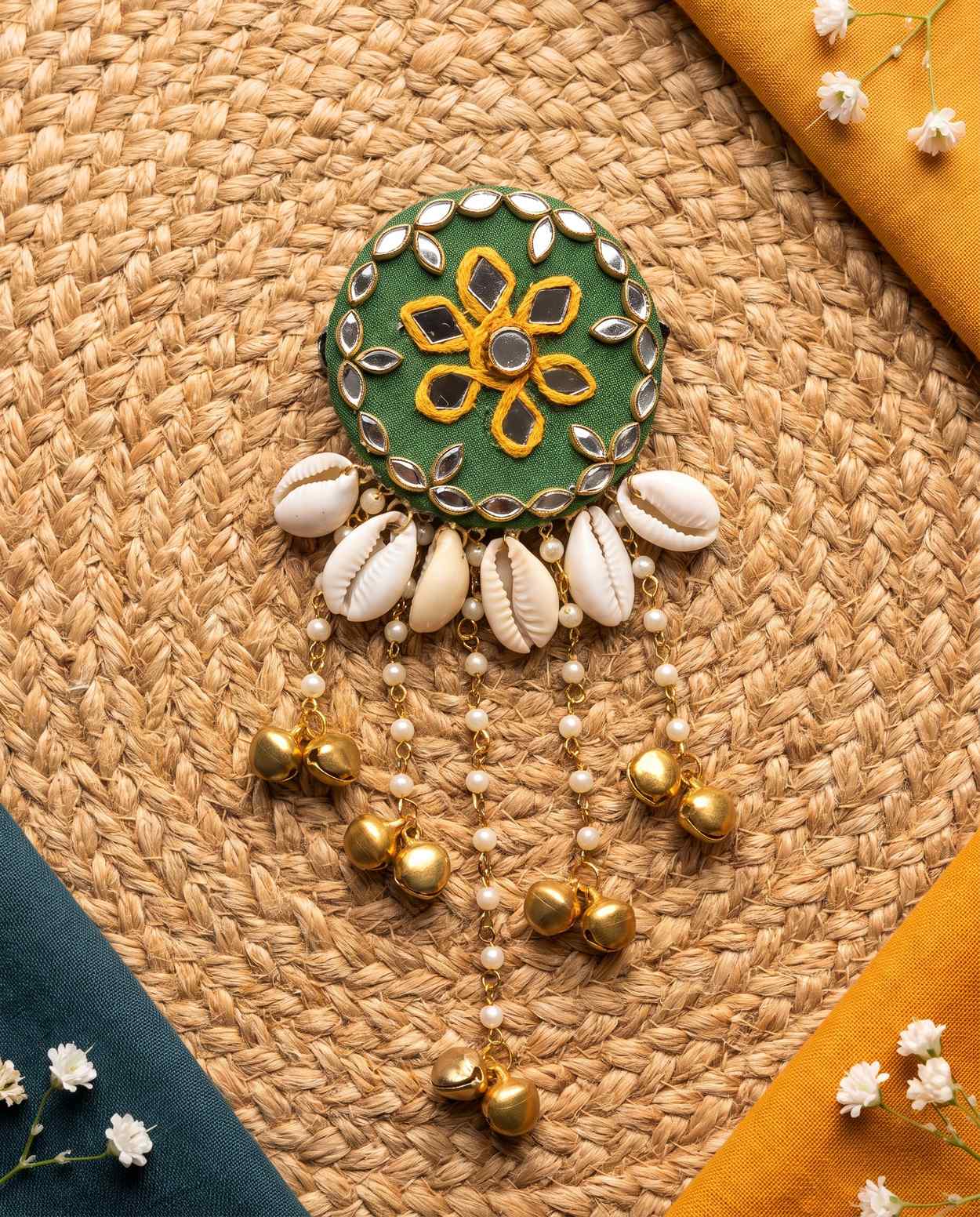 Green mirror hair brooch with shell tassels styled on jute mat with teal and mustard fabric