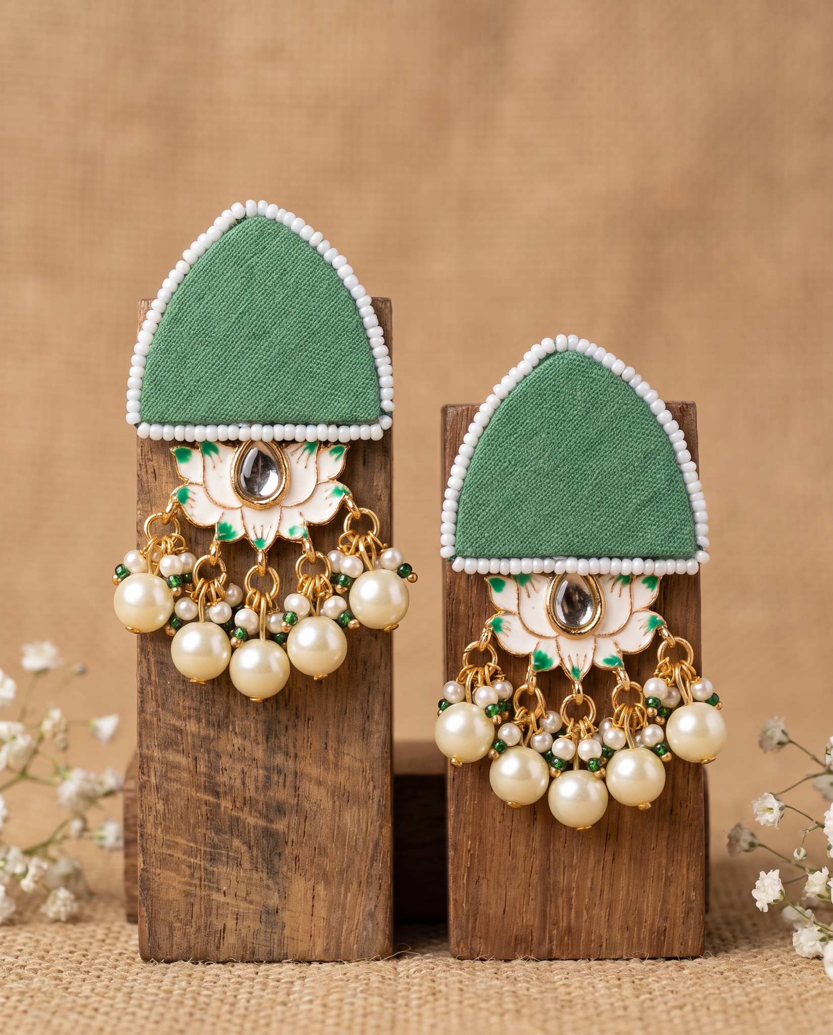 Pair of green floral earrings with pearl drops displayed on wood blocks