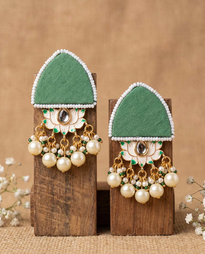 Pair of green floral earrings with pearl drops displayed on wood blocks