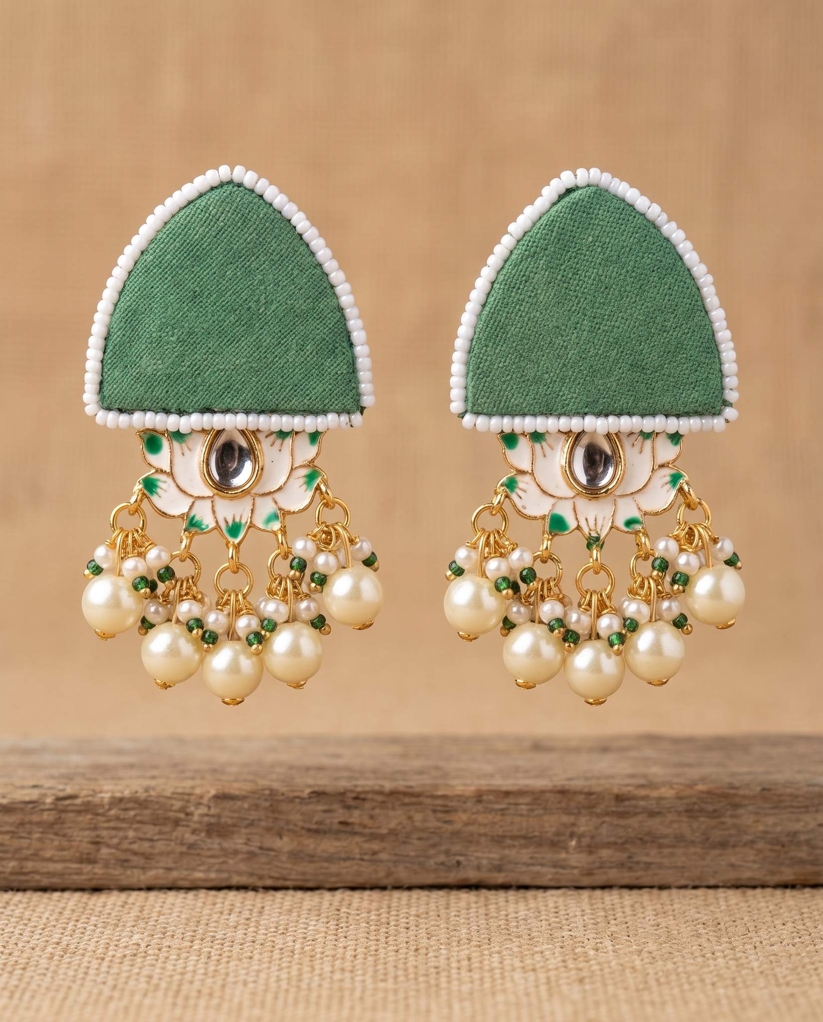 Green fabric floral earrings with pearl tassels hanging against tan backdrop