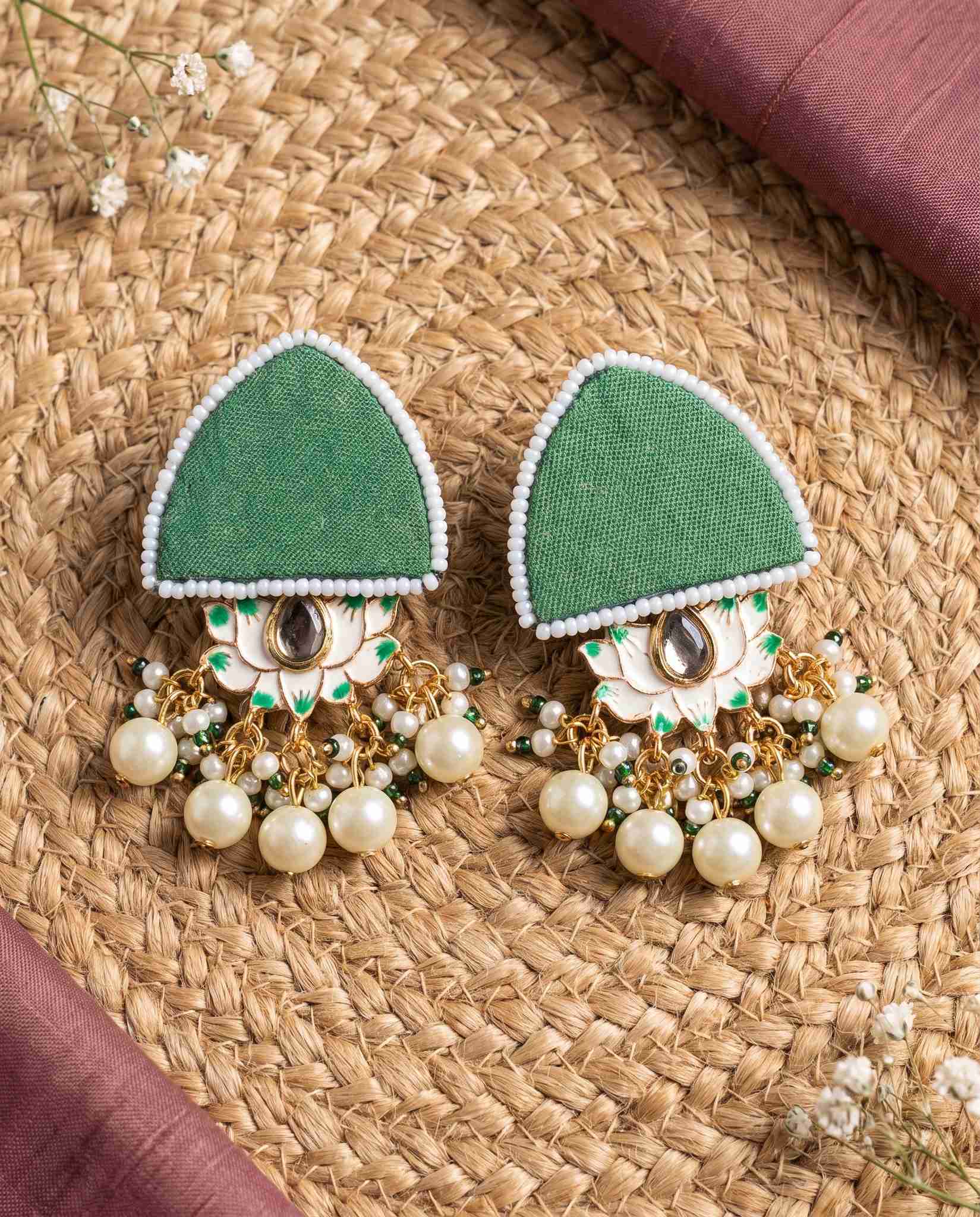 Green pearl floral earrings styled on jute mat with mauve fabric