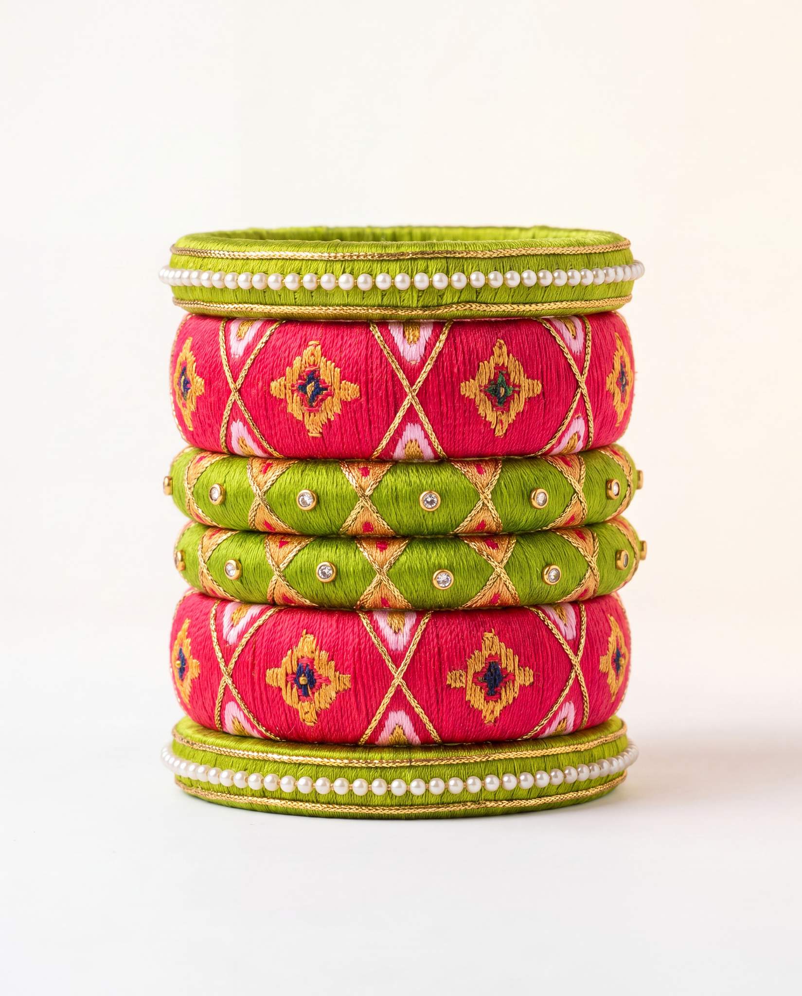 Green and pink silk thread bangle set with bandhani print and pearl detailing on plain background