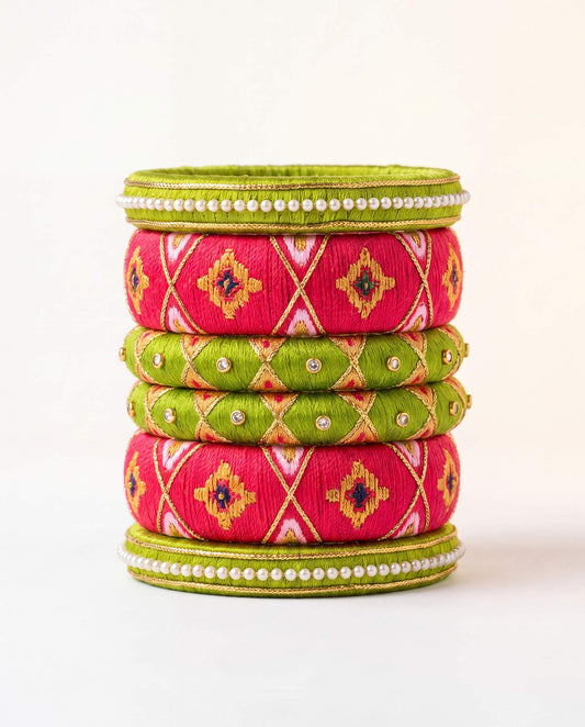 Green and pink silk thread bangle set with bandhani print and pearl detailing on plain background
