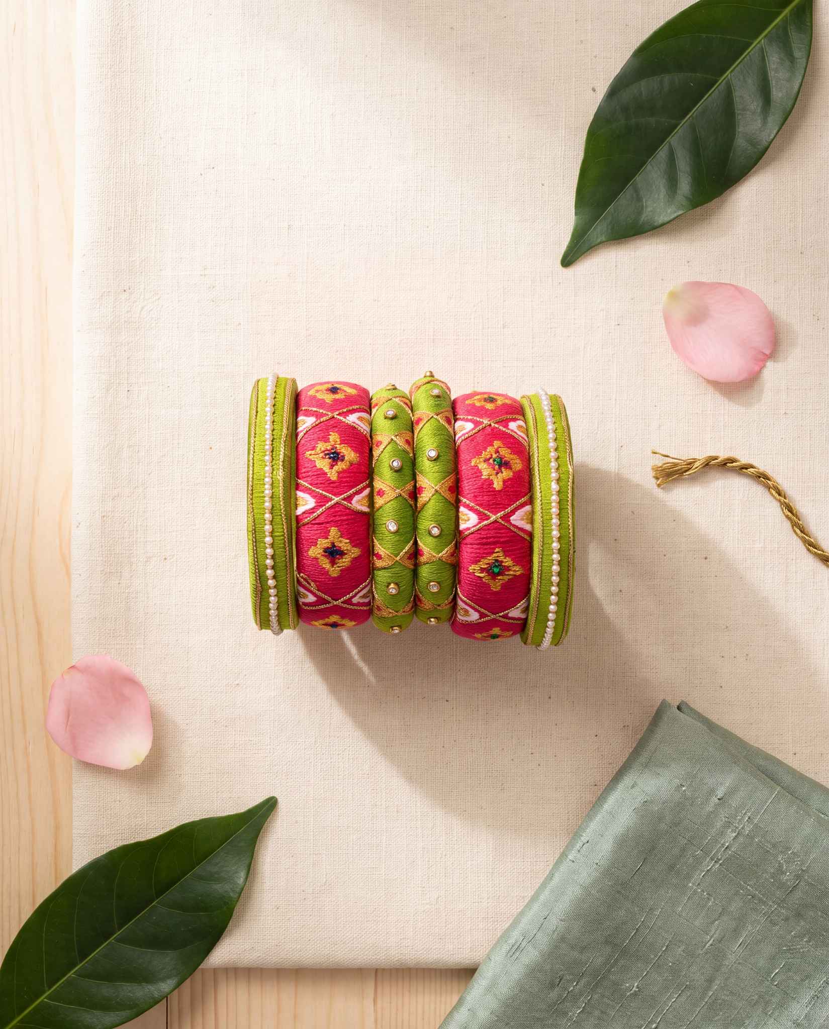 Green and pink bandhani bangles styled with leaves and pink petals on cream linen