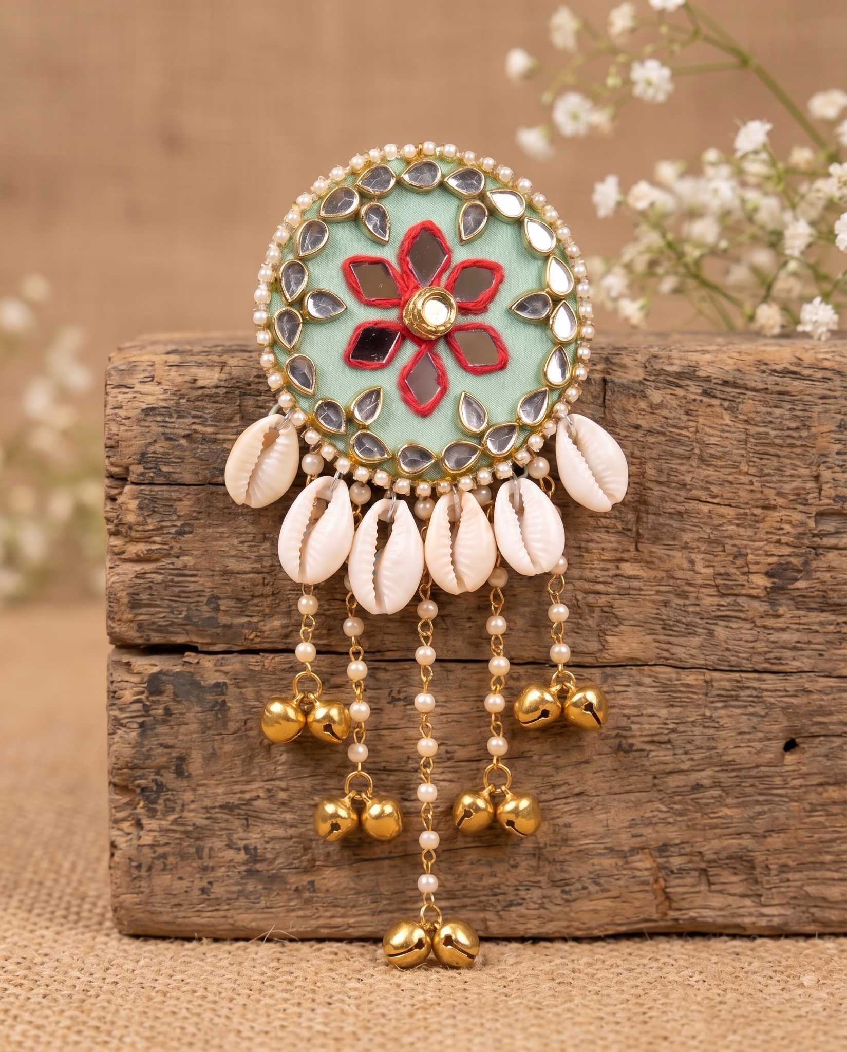 Mint green mirror hair brooch with shell and bell fringe displayed on wood block with flowers