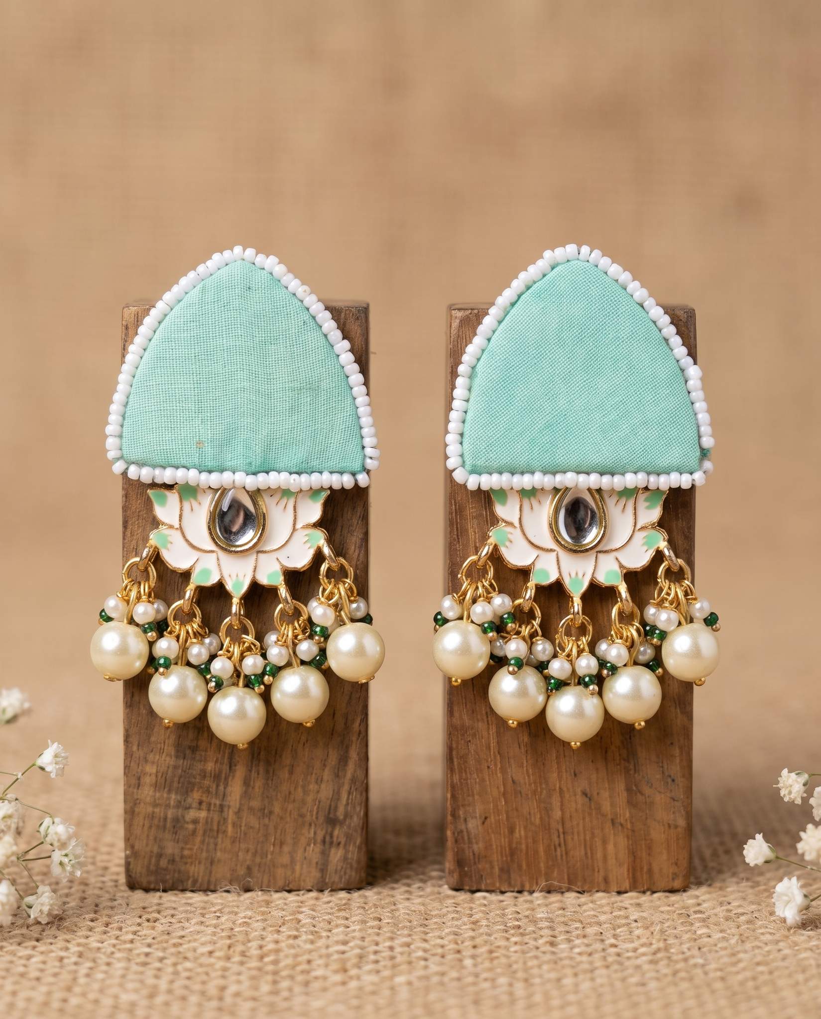 Pair of mint green floral earrings with pearl drops displayed on wood blocks