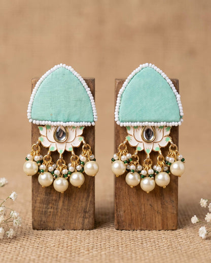 Pair of mint green floral earrings with pearl drops displayed on wood blocks
