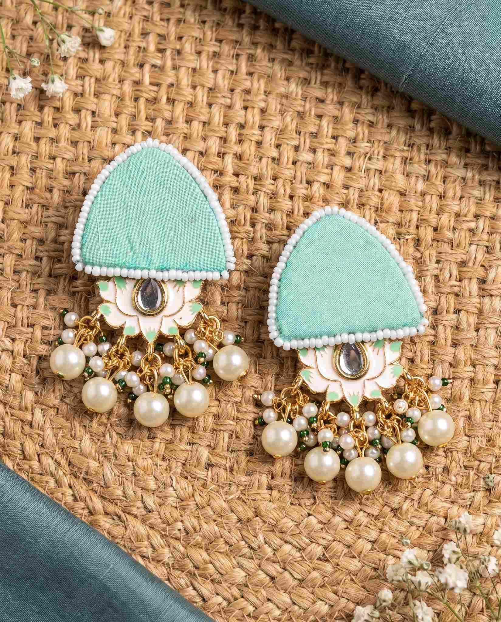 Mint green pearl floral earrings styled on jute mat with teal fabric