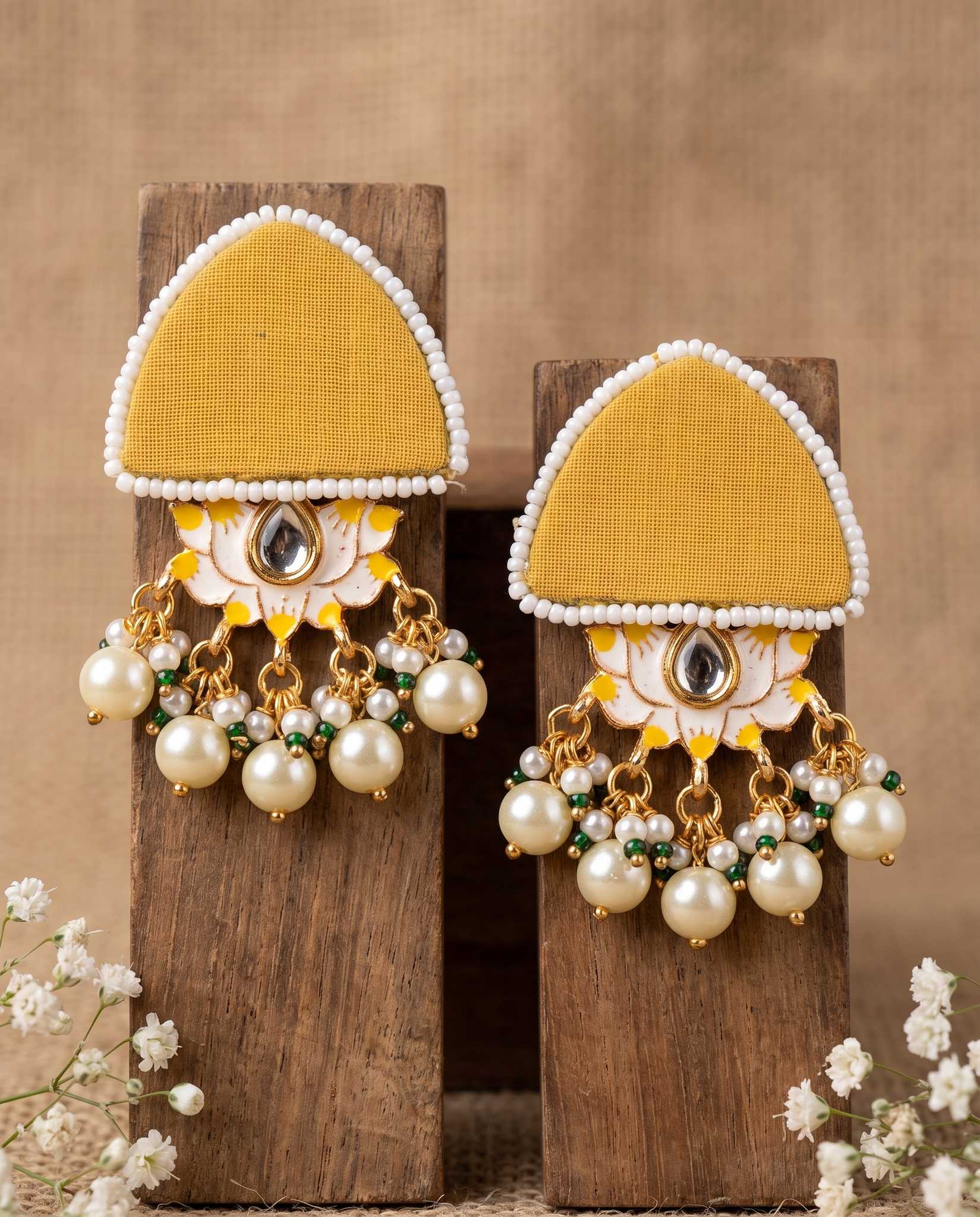Pair of mustard yellow floral earrings with pearl drops displayed on wood blocks