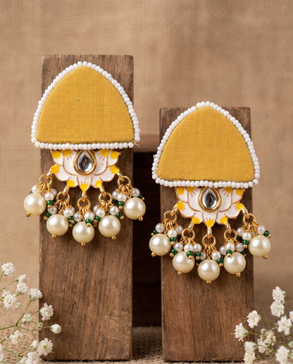 Pair of mustard yellow floral earrings with pearl drops displayed on wood blocks