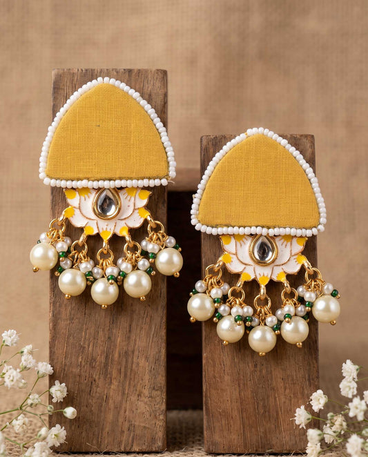 Pair of mustard yellow floral earrings with pearl drops displayed on wood blocks