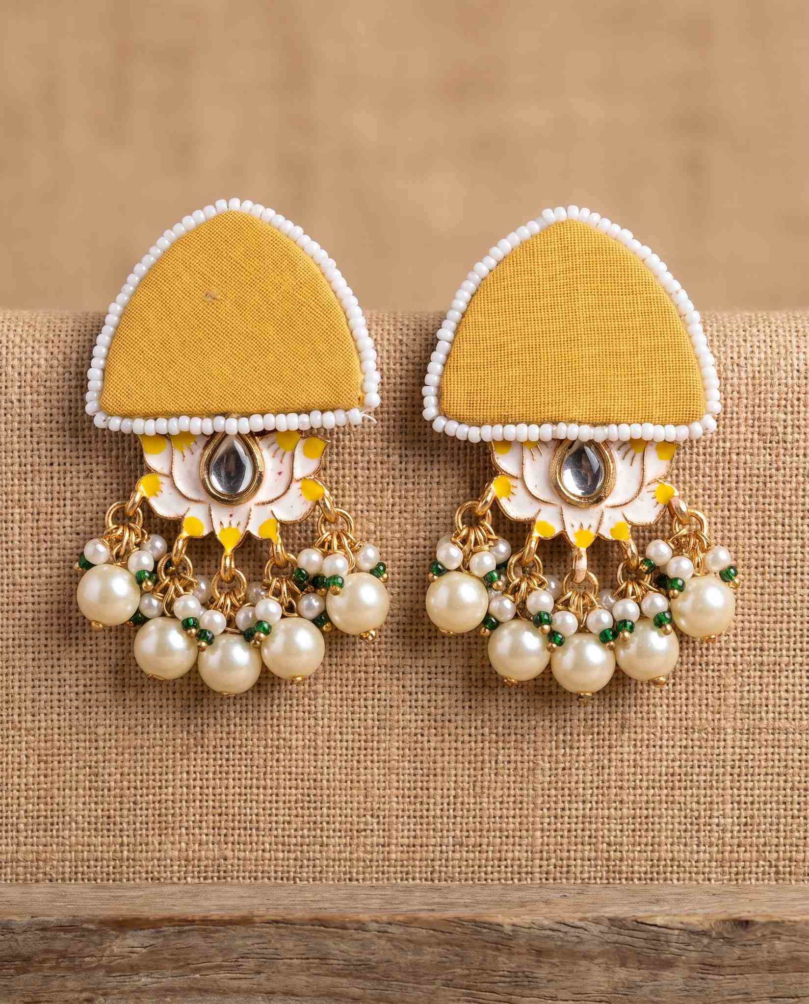 Mustard yellow fabric floral earrings with pearl tassels on jute weave background