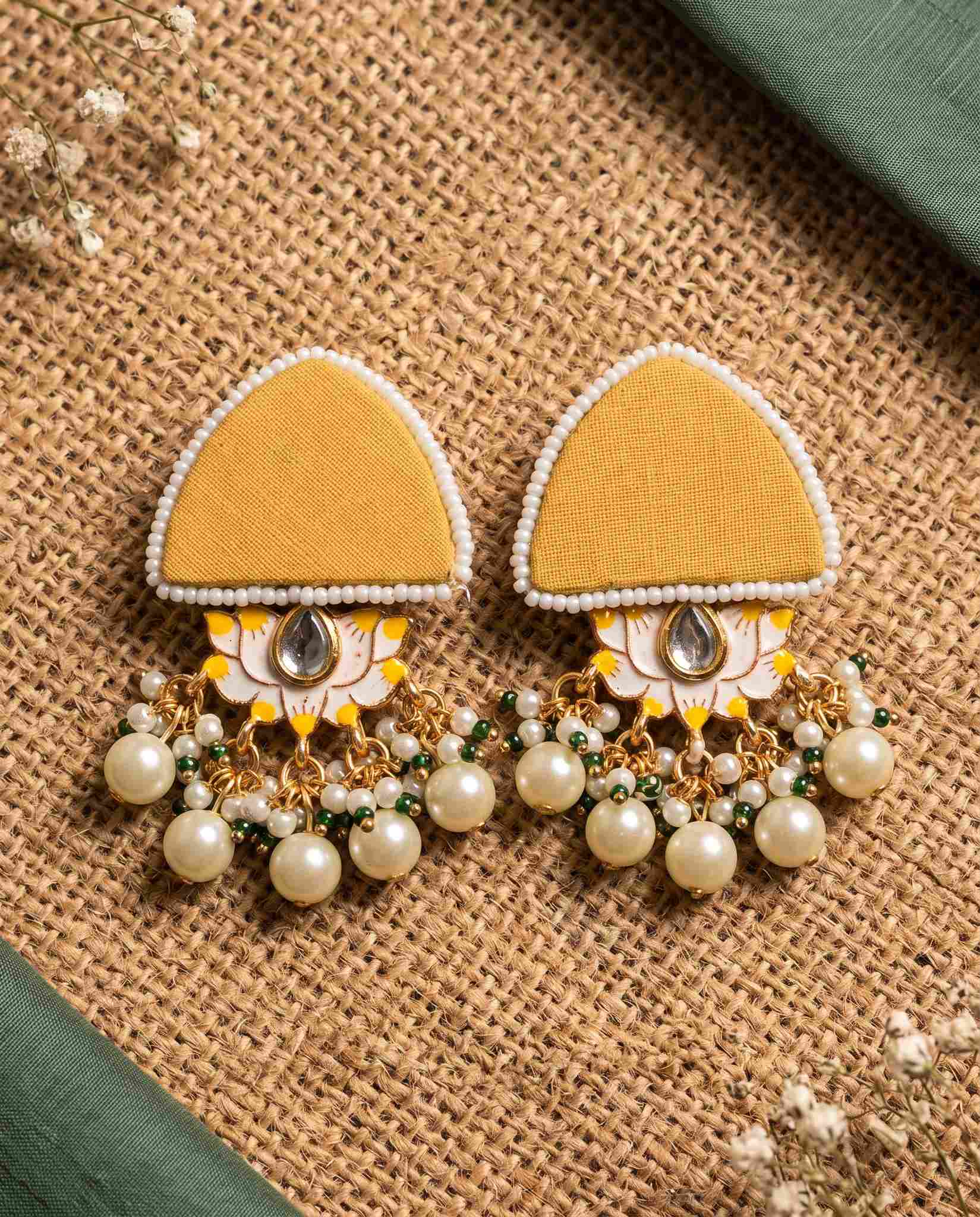 Mustard yellow pearl floral earrings styled on jute mat with green fabric