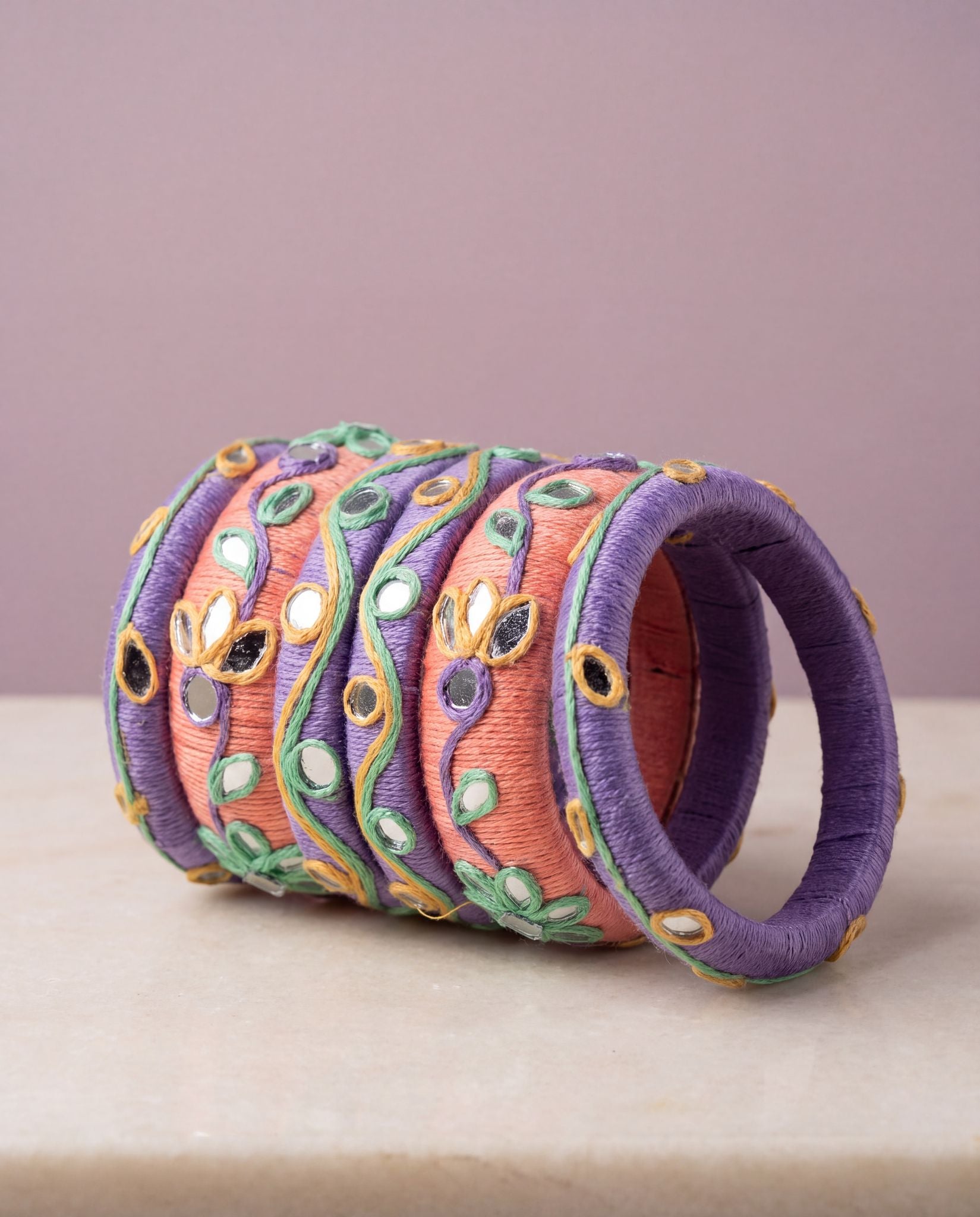 Side angle view of peach and purple silk thread bangles showing mirror and floral thread detailing