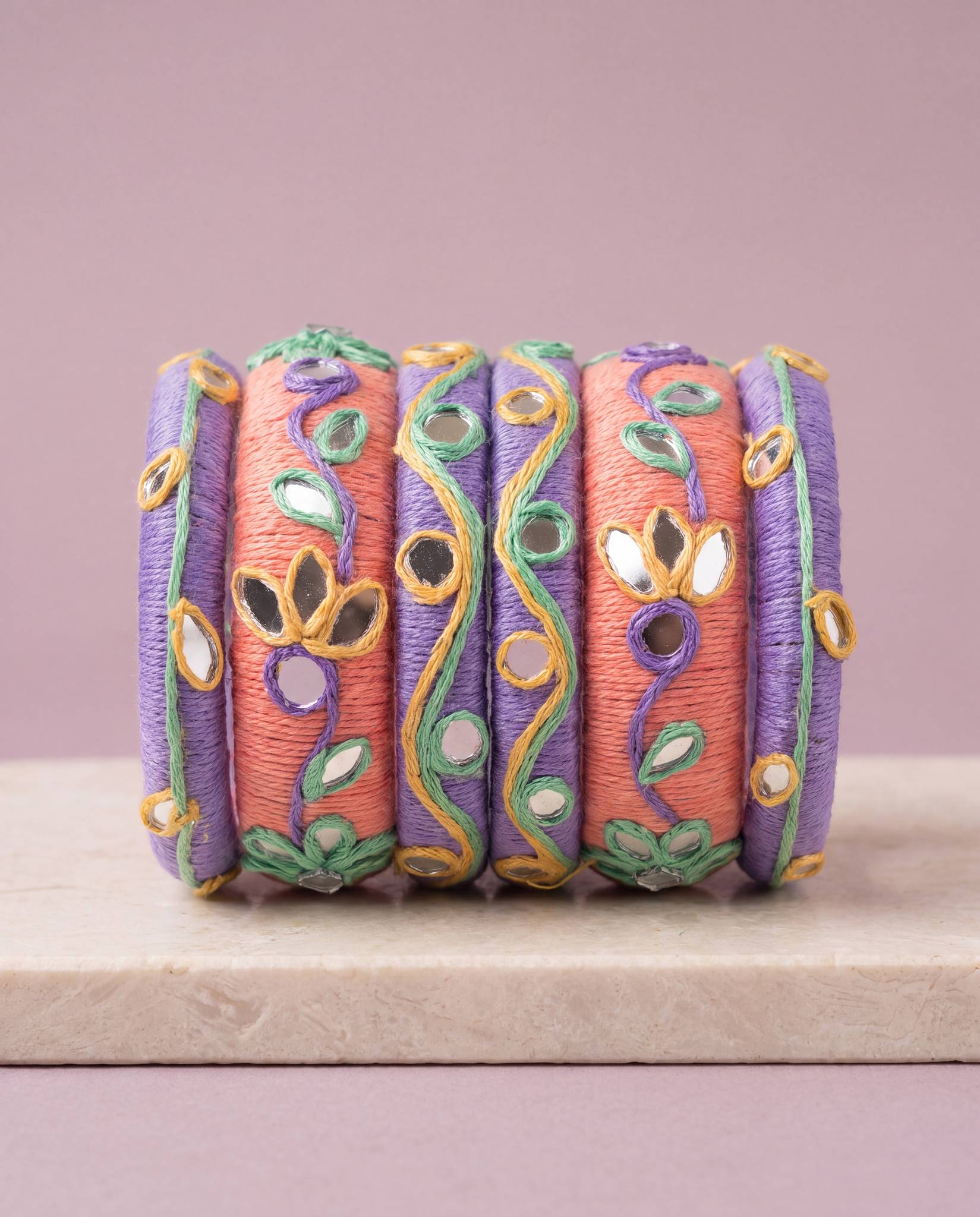 Peach and purple thread bangles with mirror work displayed against a mauve background