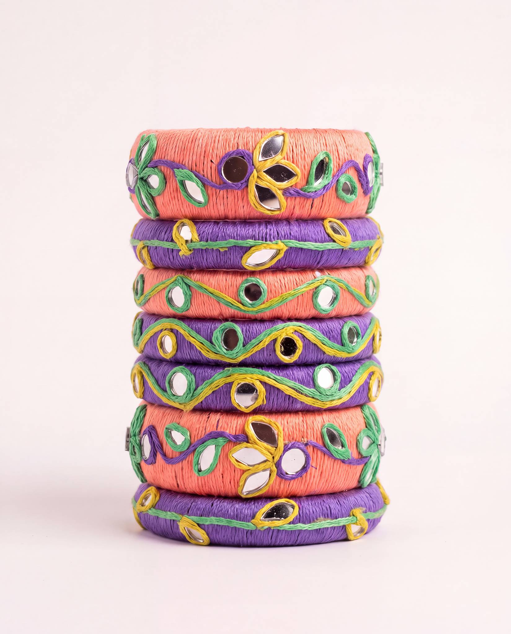 Peach and purple thread bangle set with mirror work and green floral embroidery on plain background