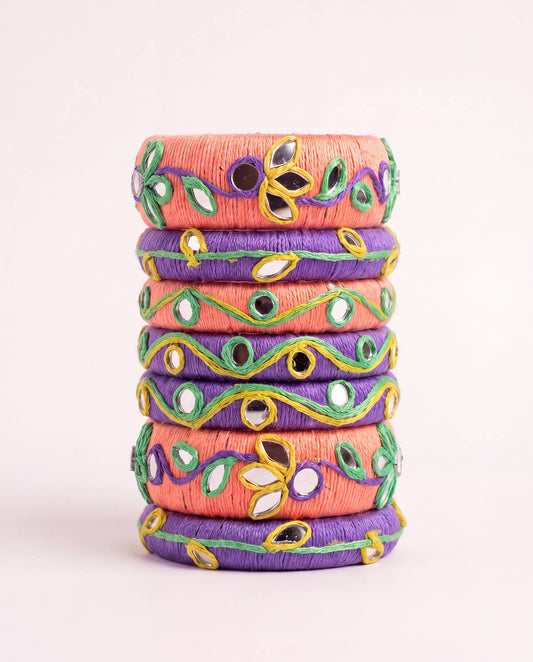 Peach and purple thread bangle set with mirror work and green floral embroidery on plain background