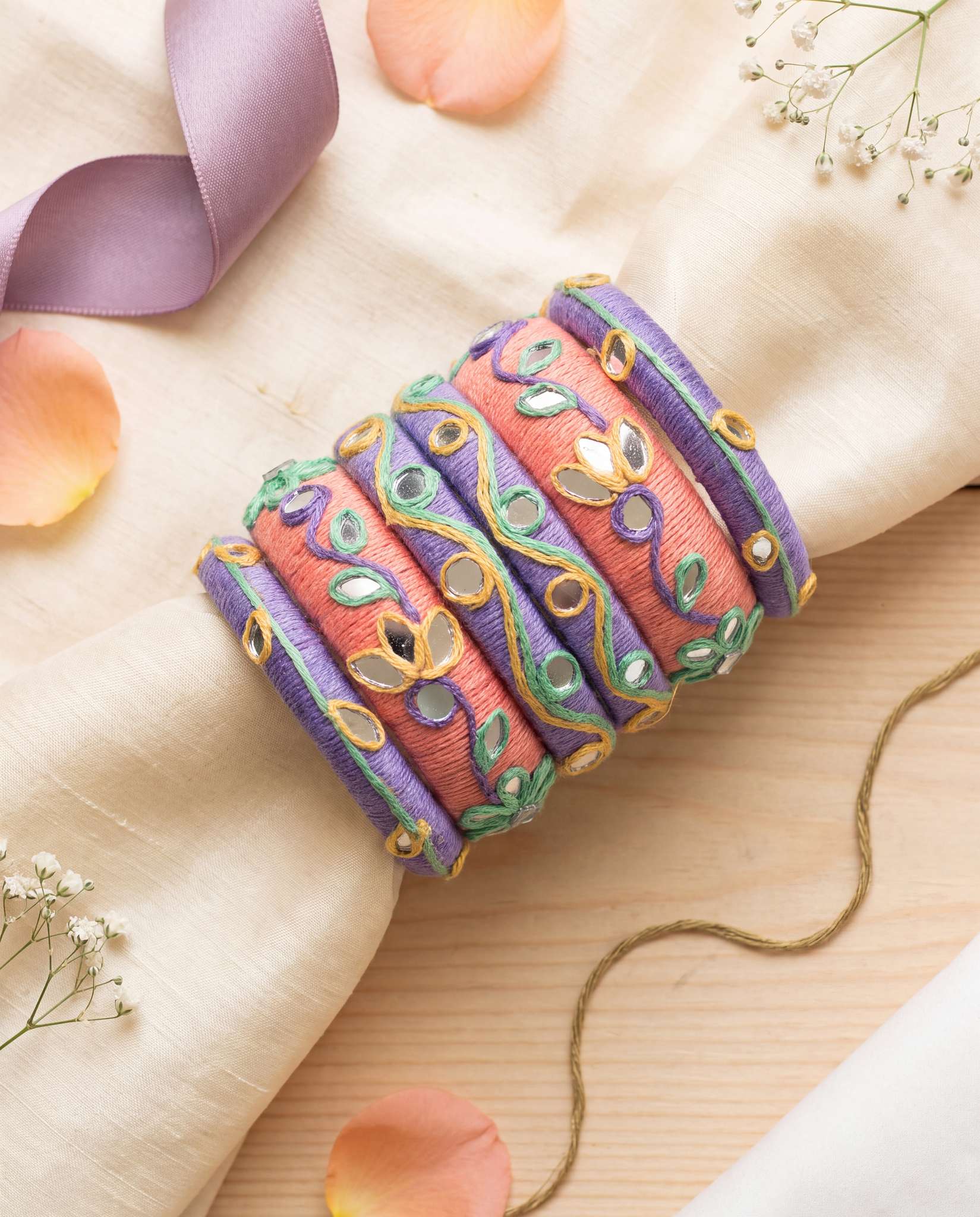 Peach and purple thread bangles styled with lavender ribbon and flower petals on fabric backdrop