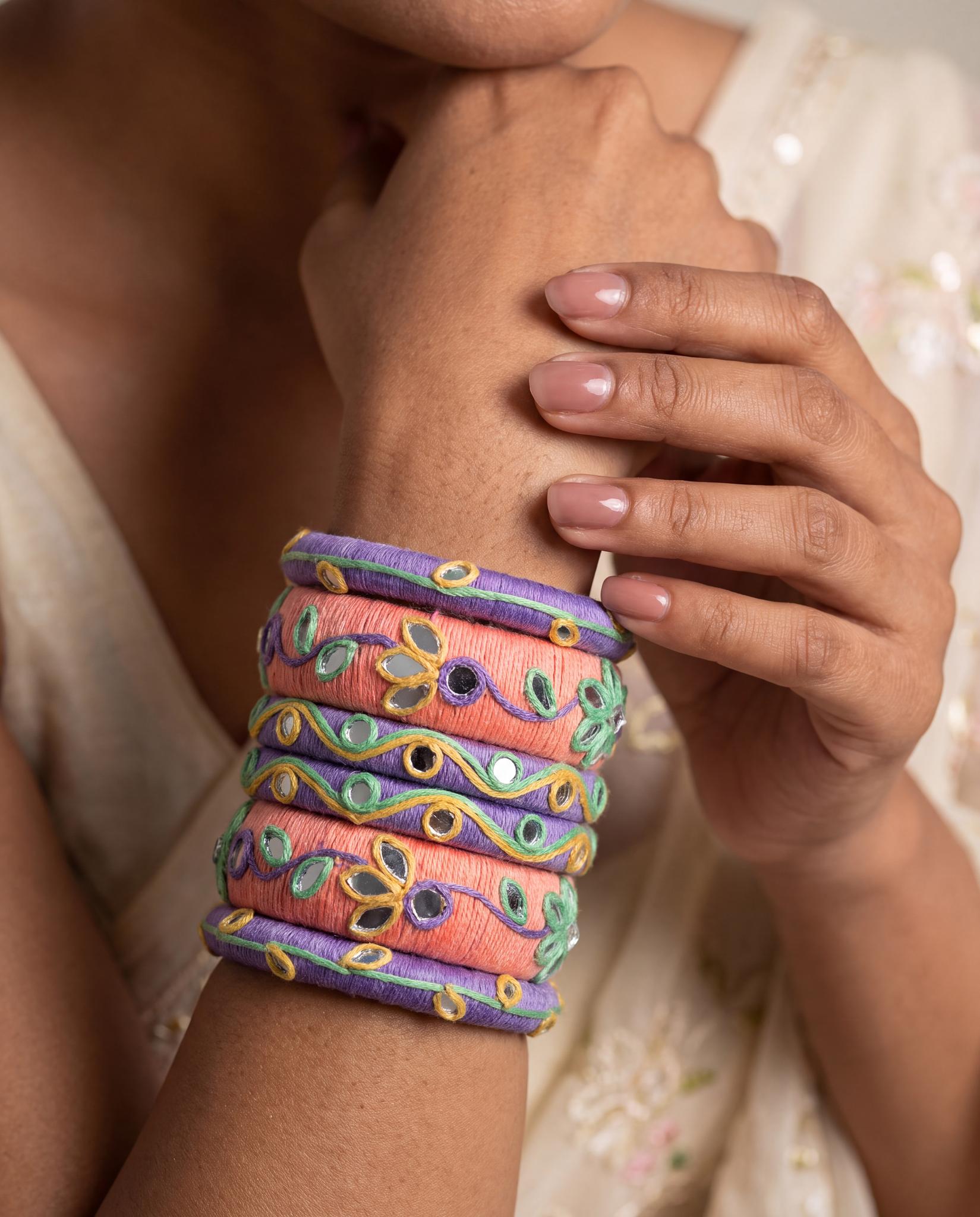 Woman wearing peach and purple mirror-work thread bangles stacked on wrist