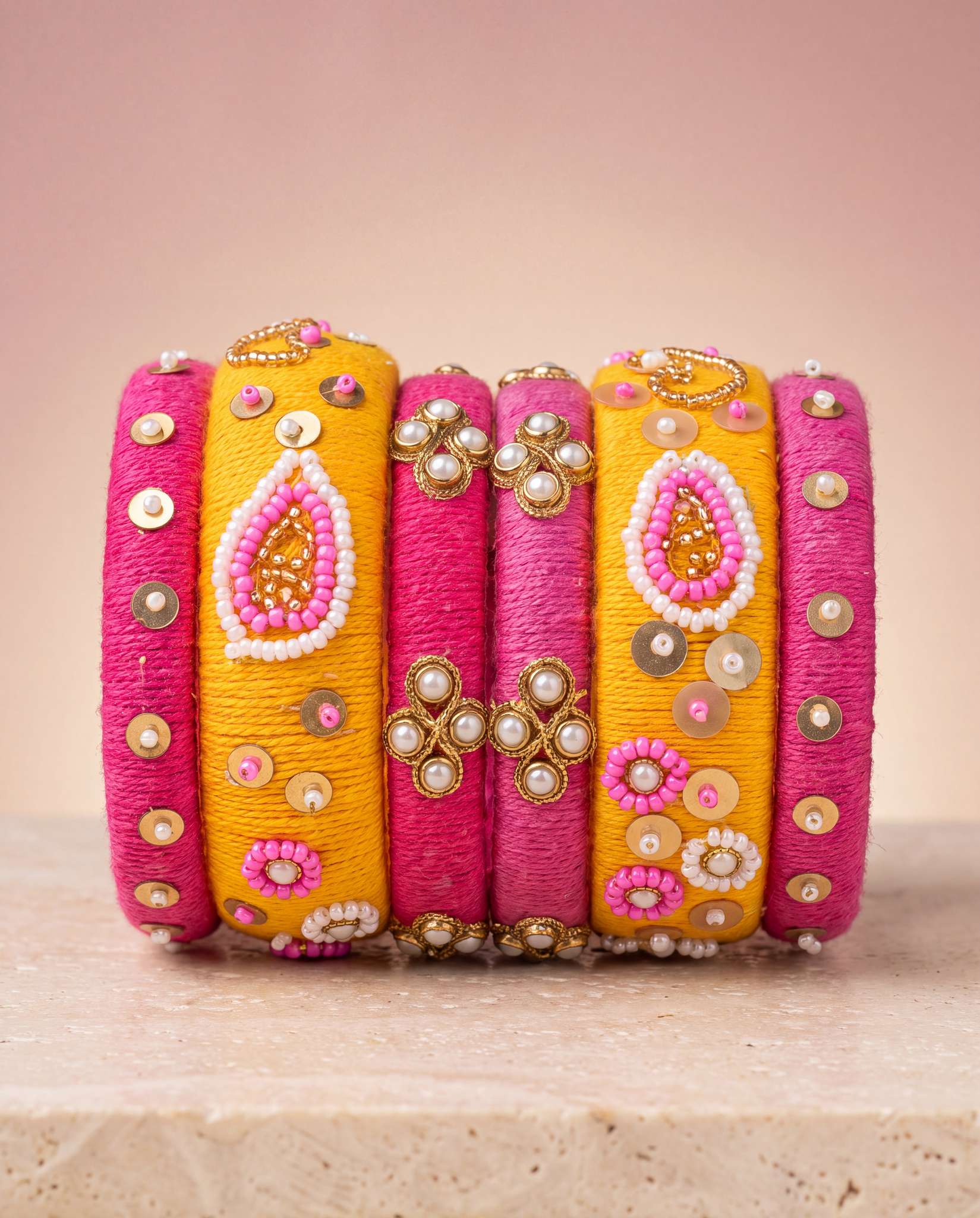 Pink and mustard silk thread bangles with gold pearl accents on blush gradient background