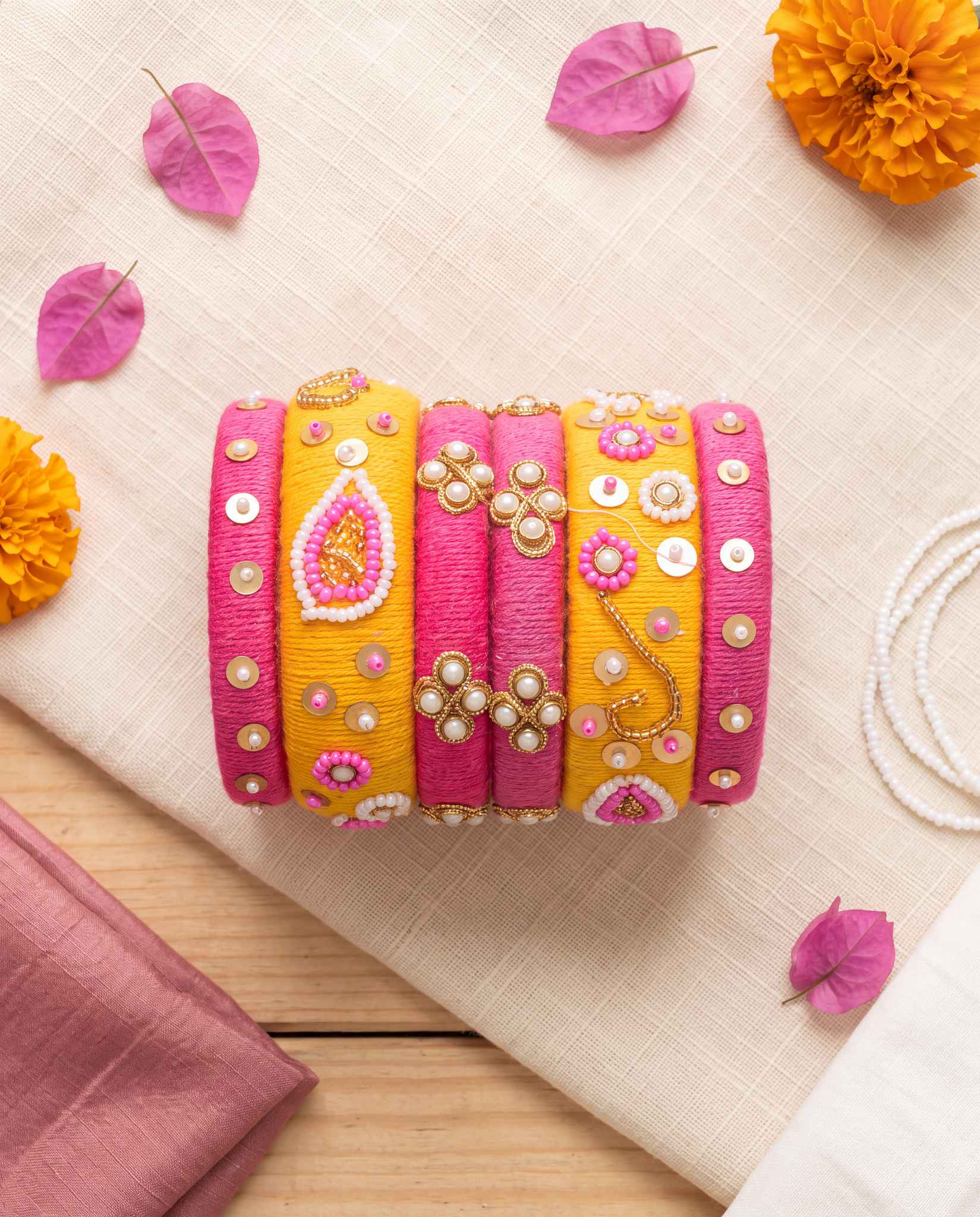 Pink and mustard floral beadwork bangles styled with marigolds and pearls on cream linen