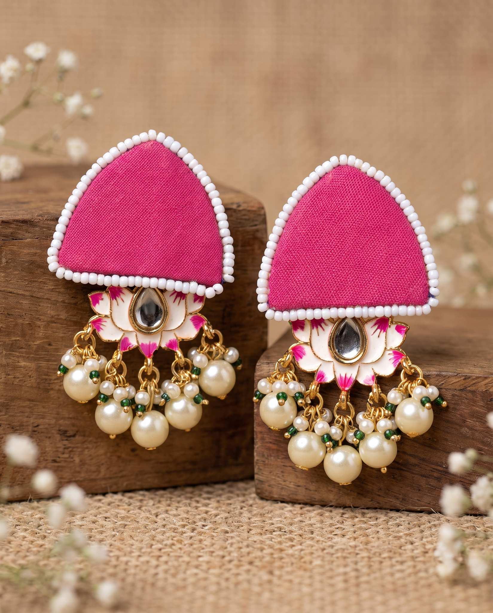 Pair of pink floral earrings with pearl drops displayed on wood blocks