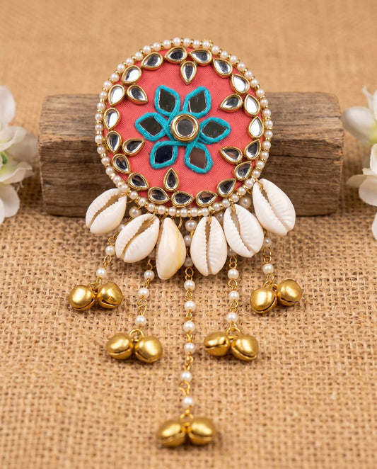 Coral mirror hair brooch with cowrie shells and gold bells displayed on wood block with flowers