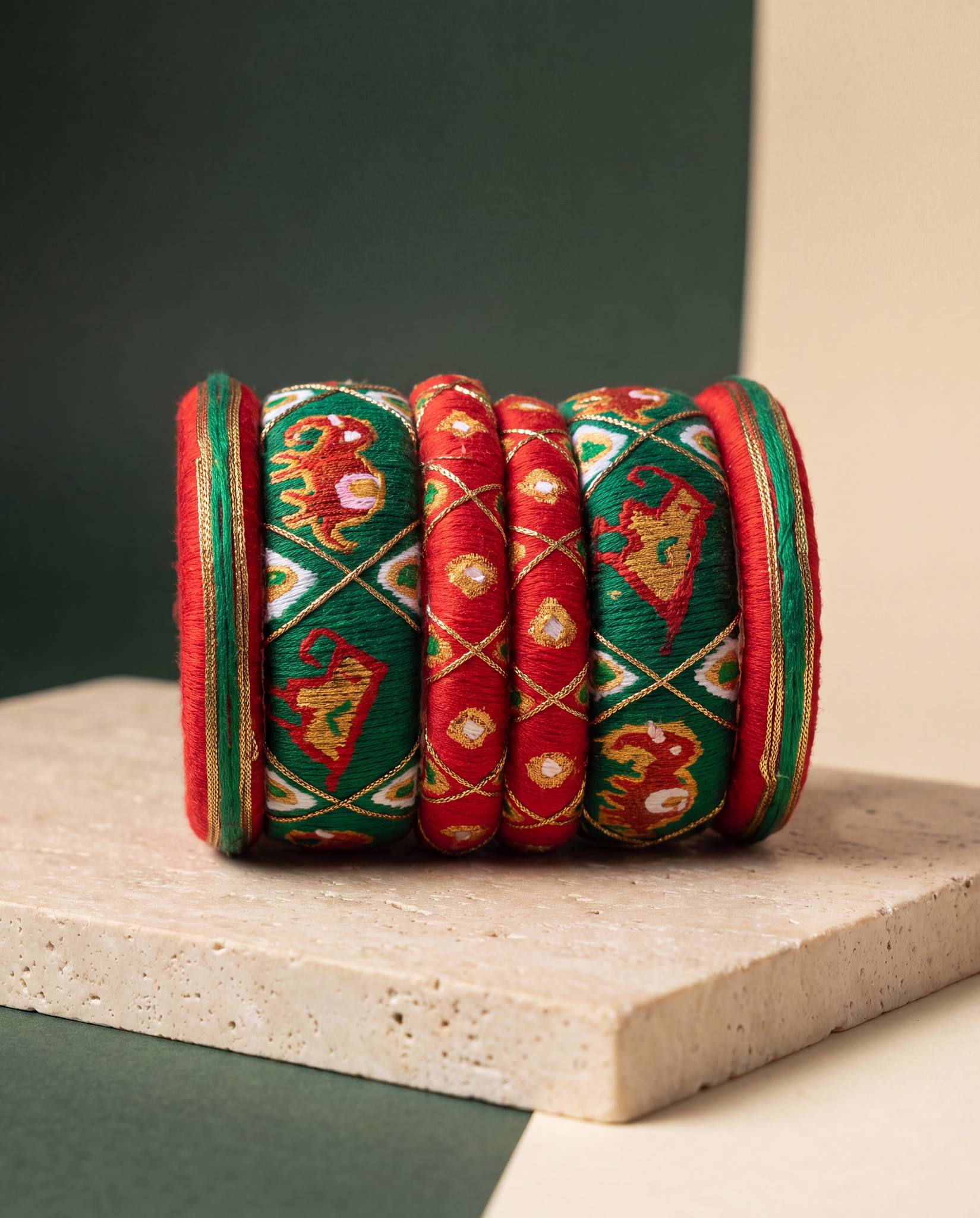 Red and green silk thread bangles with elephant embroidery displayed on stone backdrop