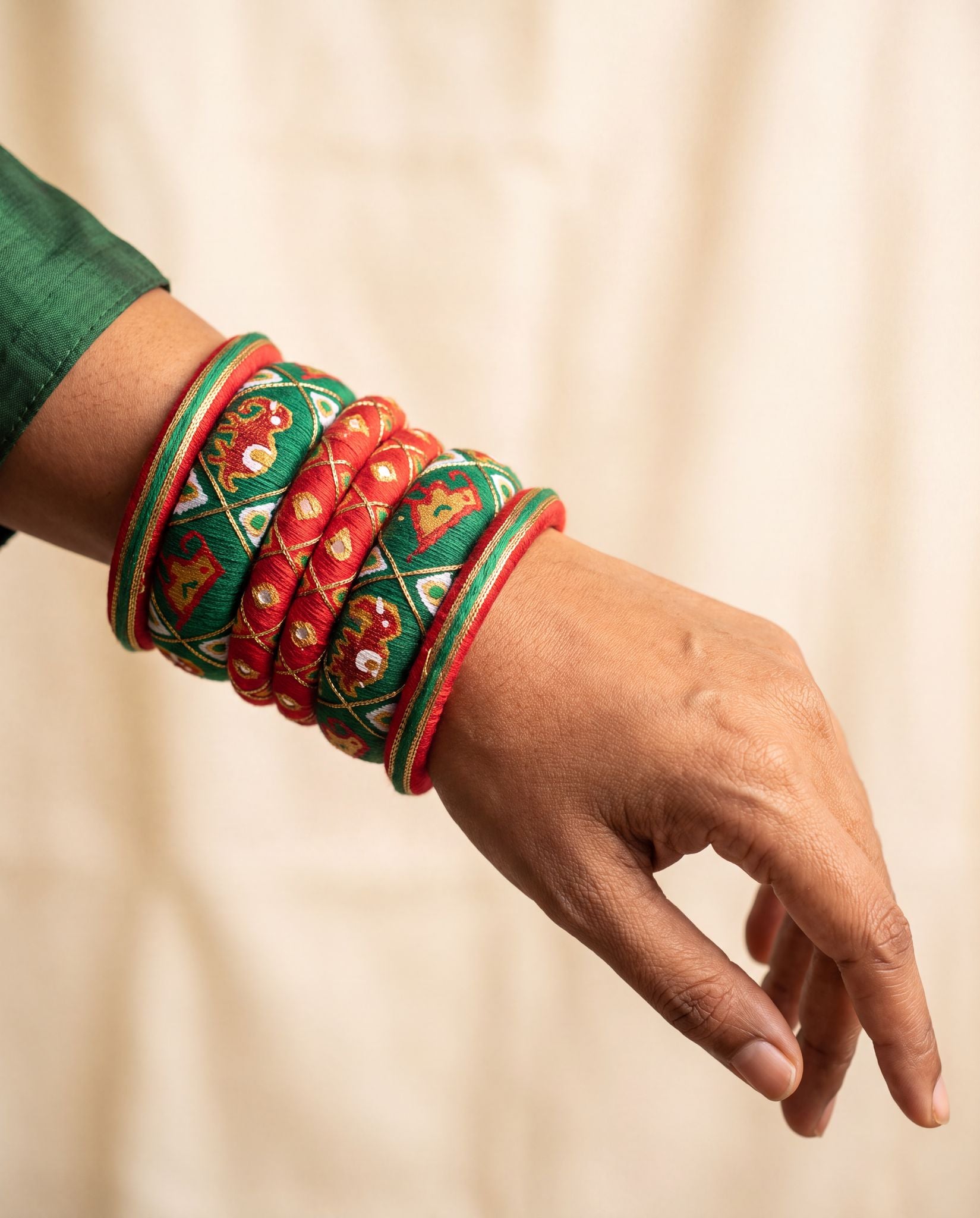 Woman wearing red and green elephant motif silk thread bangles stacked on wrist