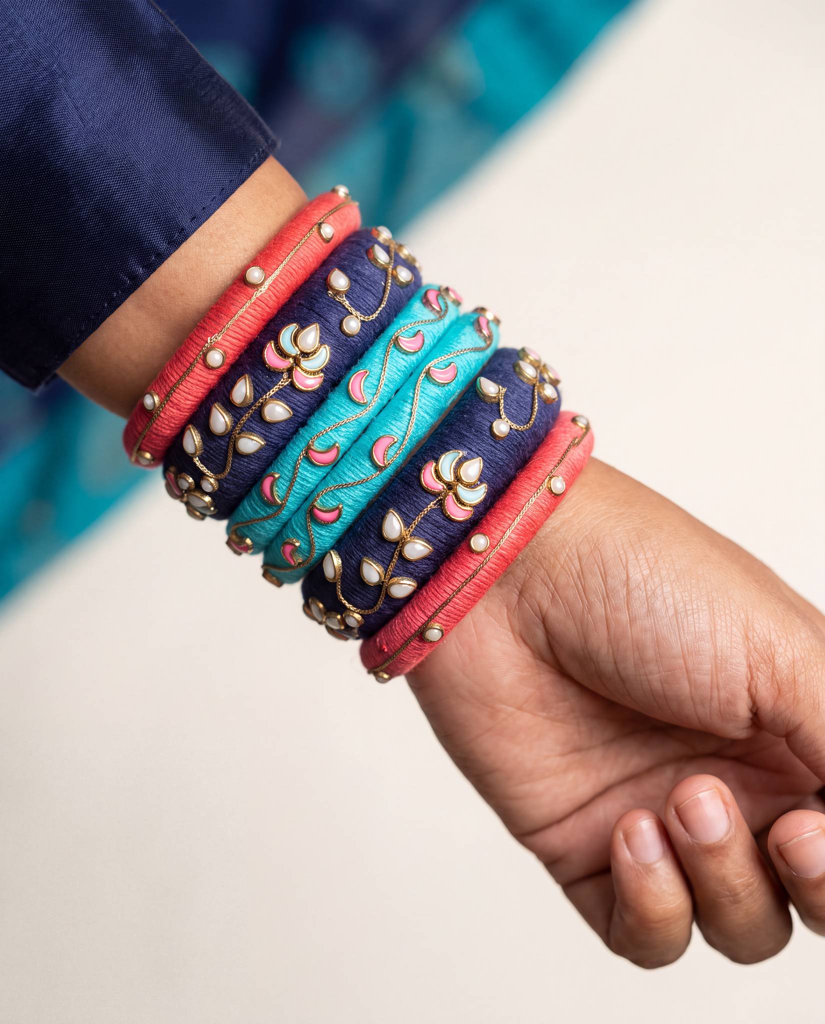 Woman wearing red, navy, and turquoise meenakari silk thread bangles stacked on wrist