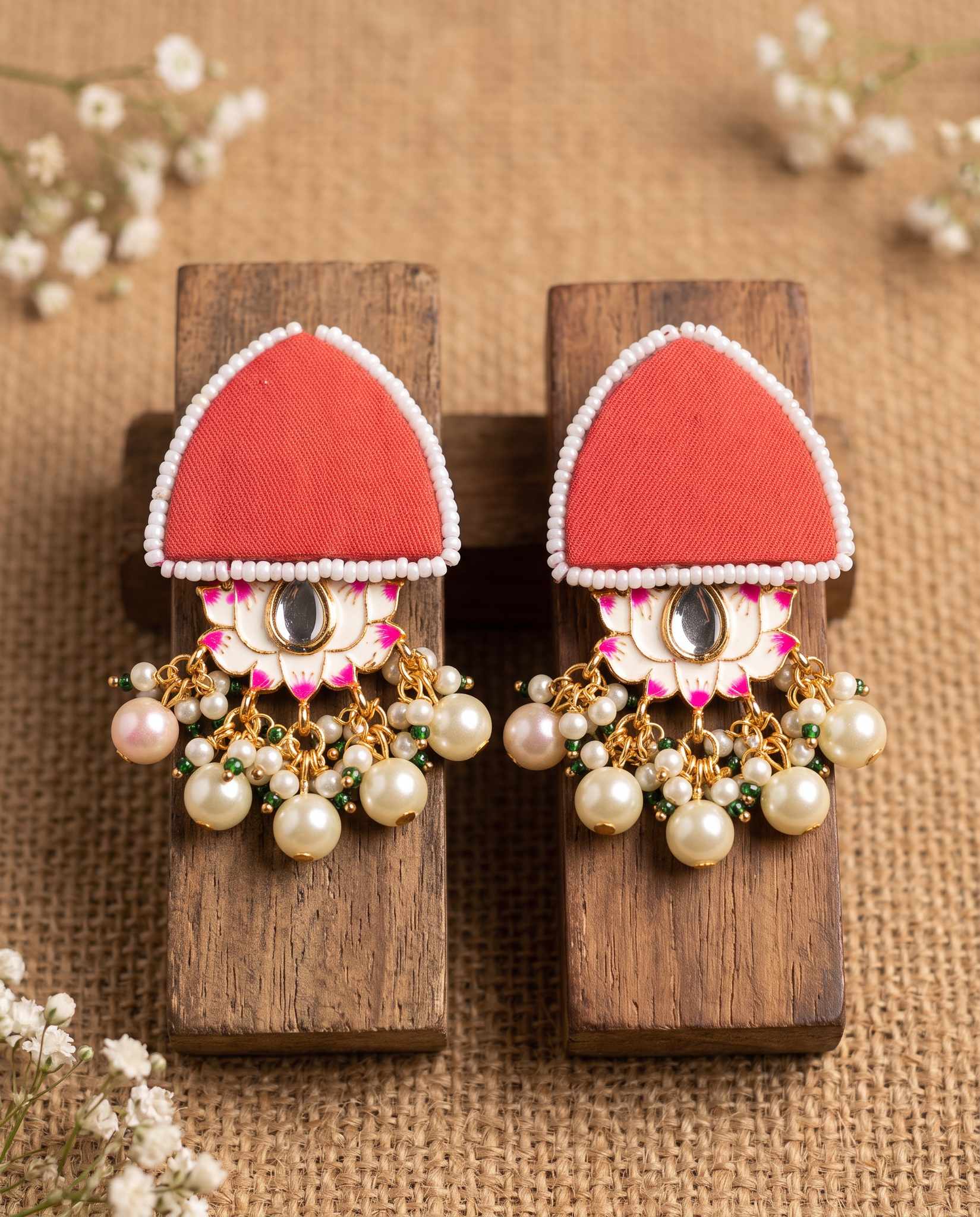 Pair of red floral earrings with pearl drops displayed on wood blocks