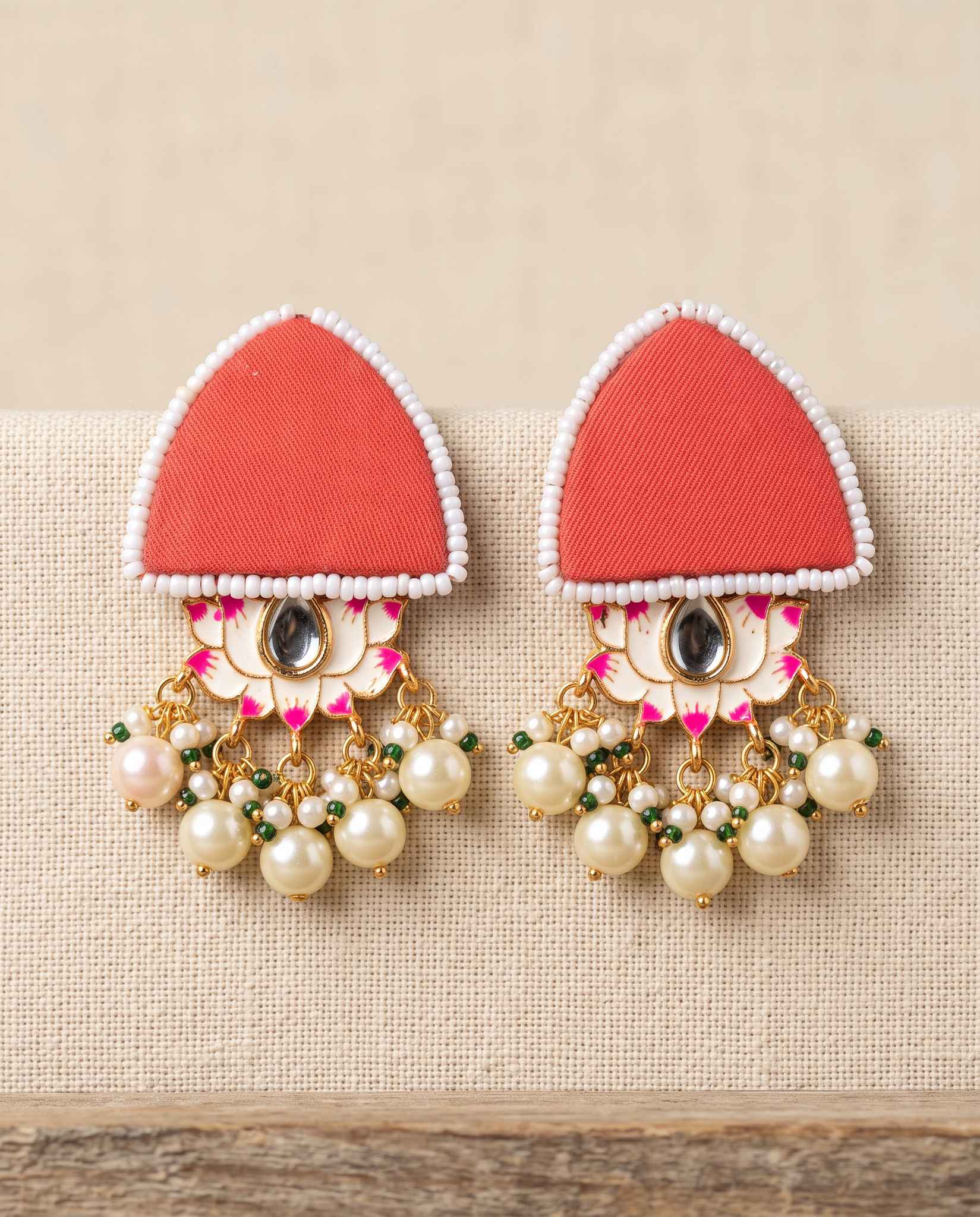 Red fabric floral earrings with pearl tassels on plain beige background