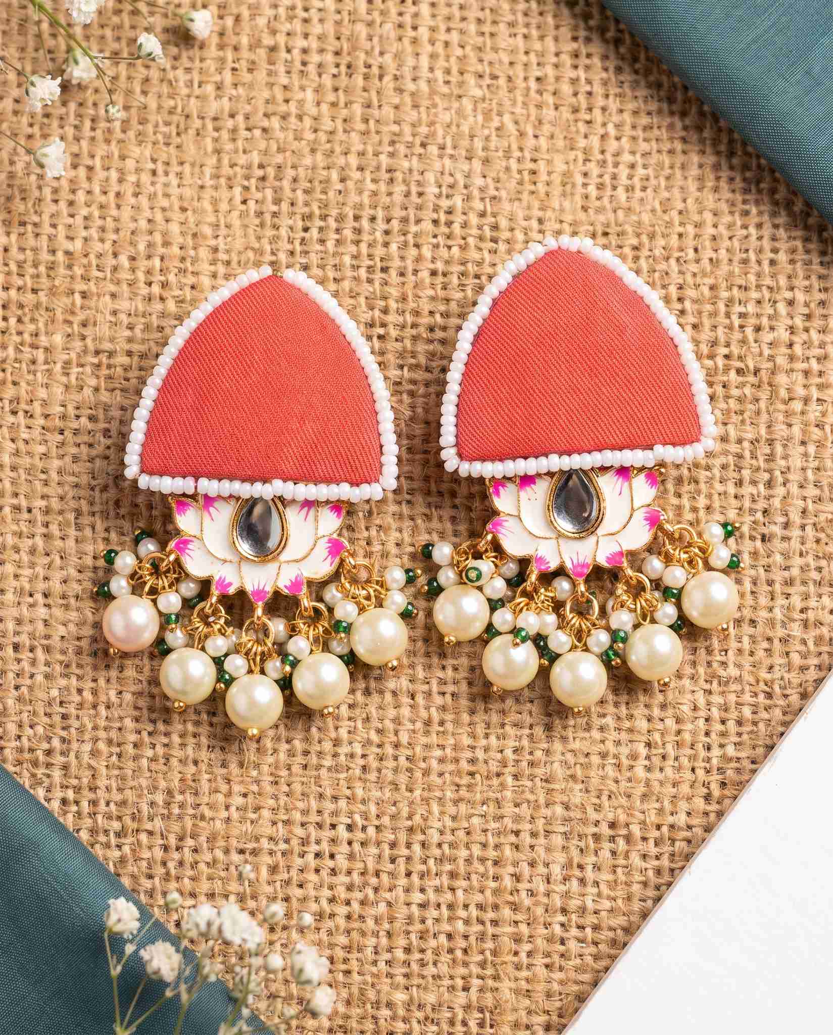 Red pearl floral earrings styled on jute mat with teal fabric