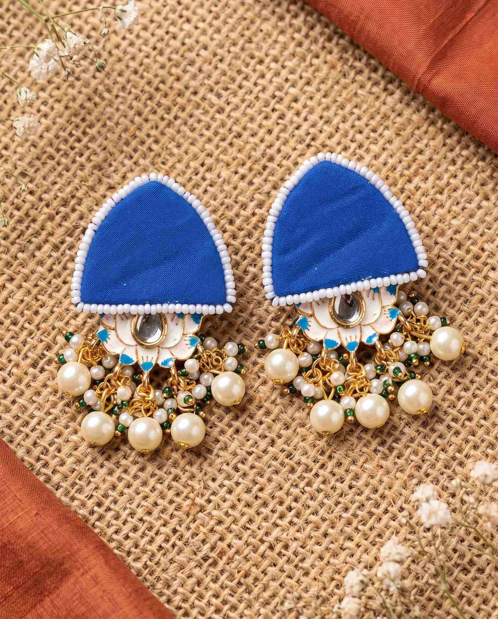 Pair of royal blue floral earrings with pearl drops displayed on wood blocks