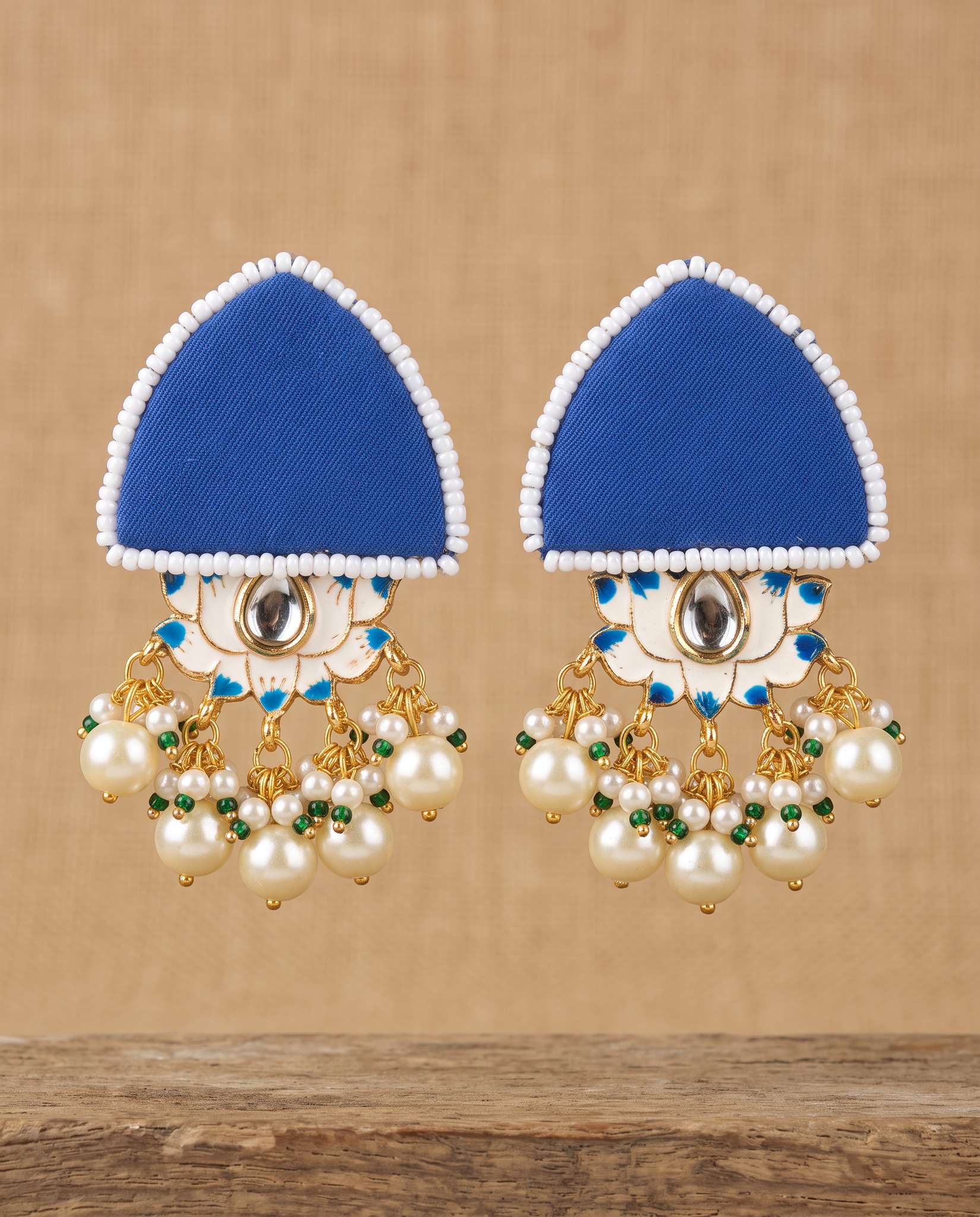 Royal blue fabric floral earrings with pearl tassels hanging against tan backdrop
