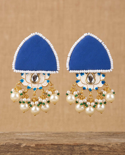 Royal blue fabric floral earrings with pearl tassels hanging against tan backdrop