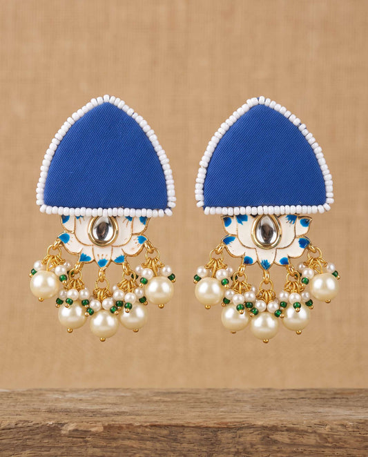 Royal blue fabric floral earrings with pearl tassels hanging against tan backdrop