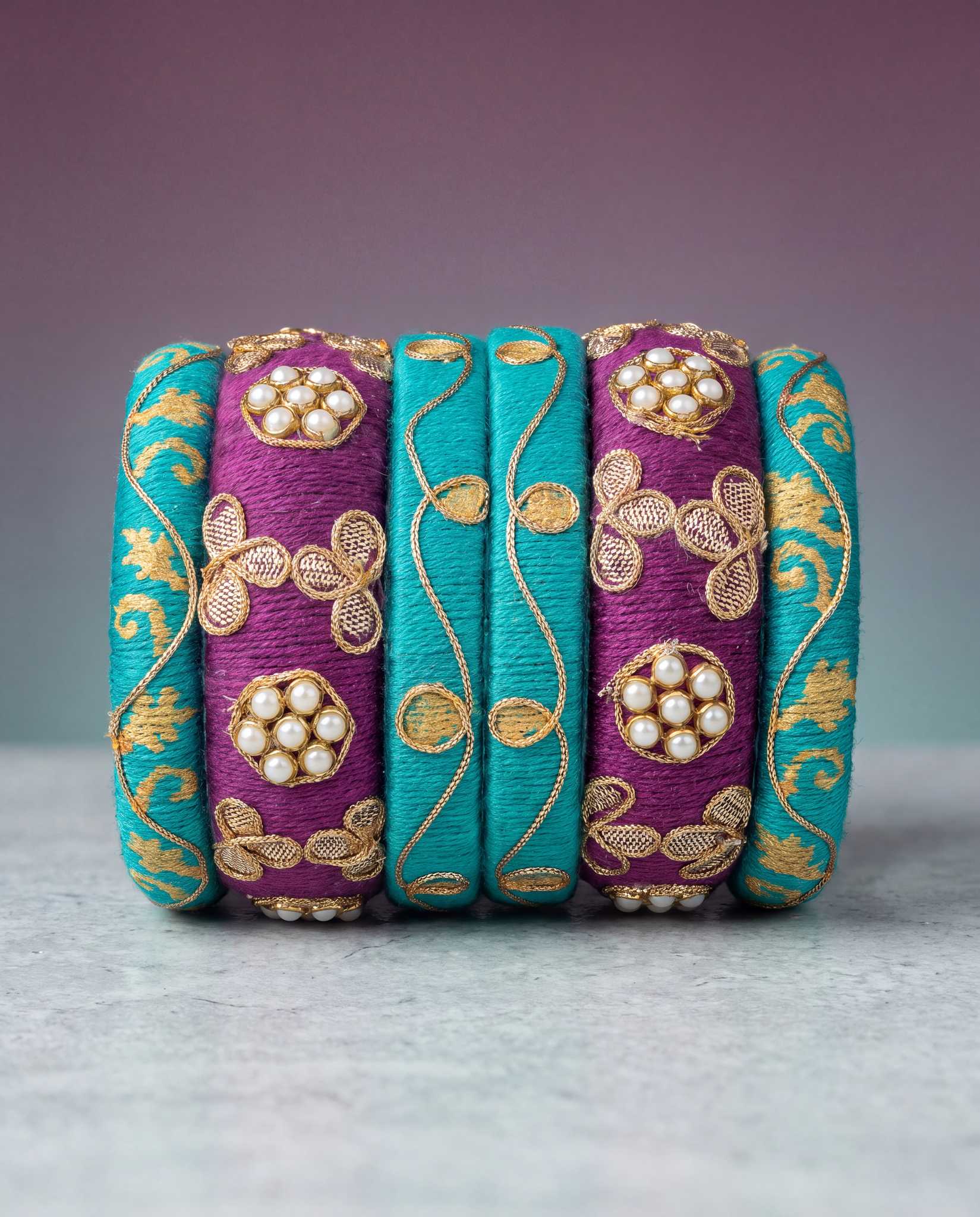 Teal and plum silk thread bangles with gold zari pattern on mauve gradient background