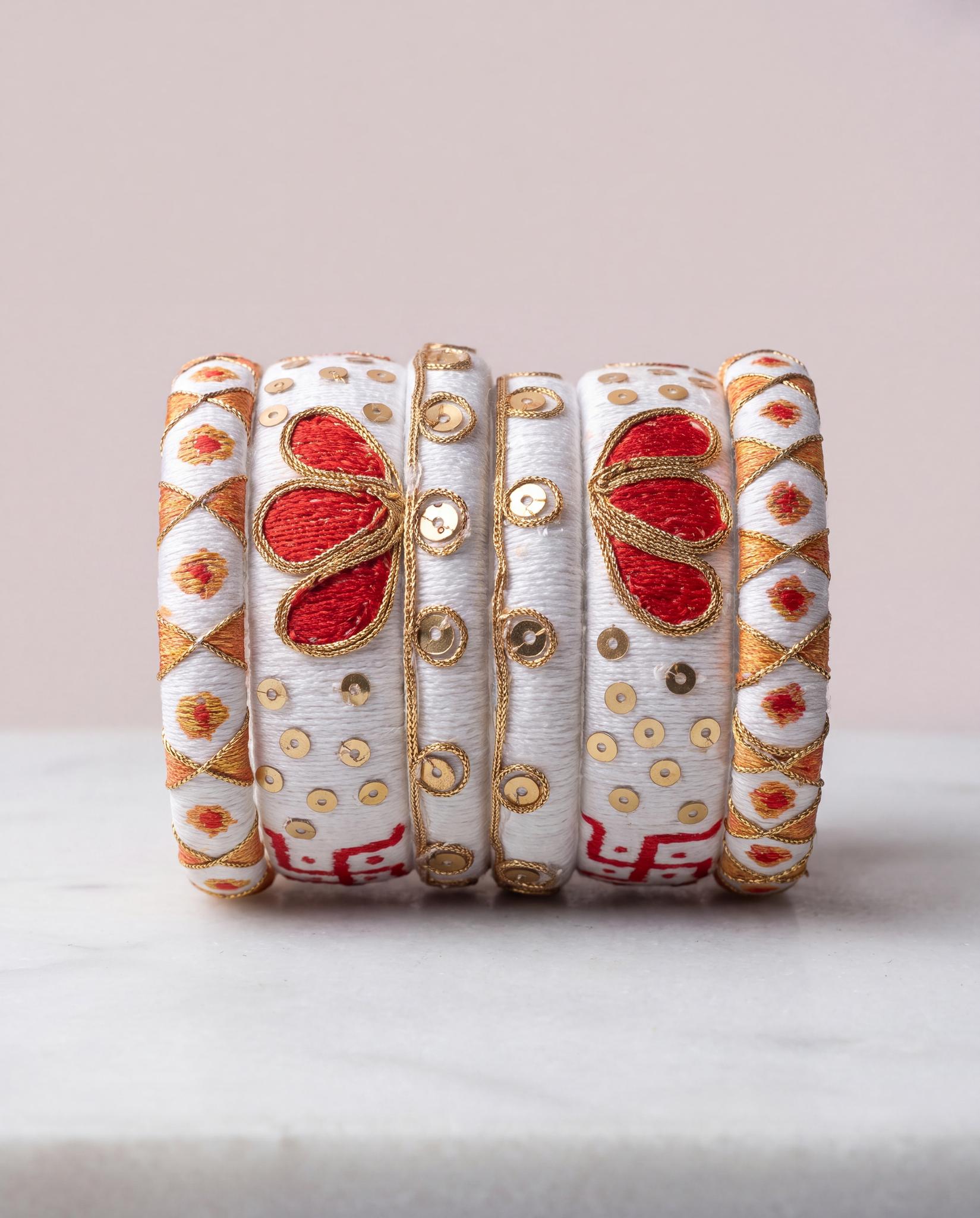 White and gold silk thread bangles with red floral motif on pale pink background