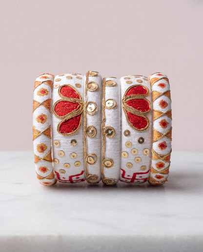 White and gold silk thread bangles with red floral motif on pale pink background