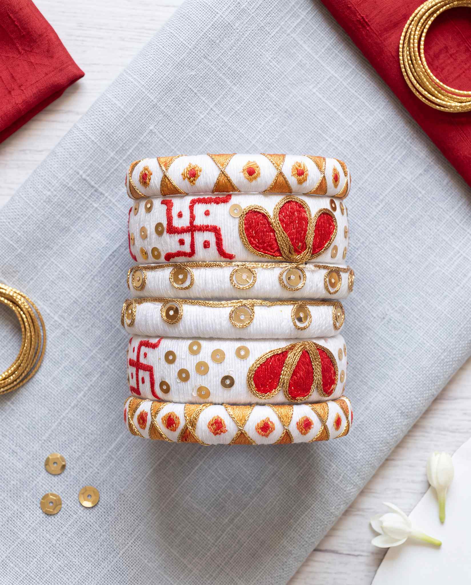 White silk thread swastik bangles styled flat lay with red napkins and gold bangles