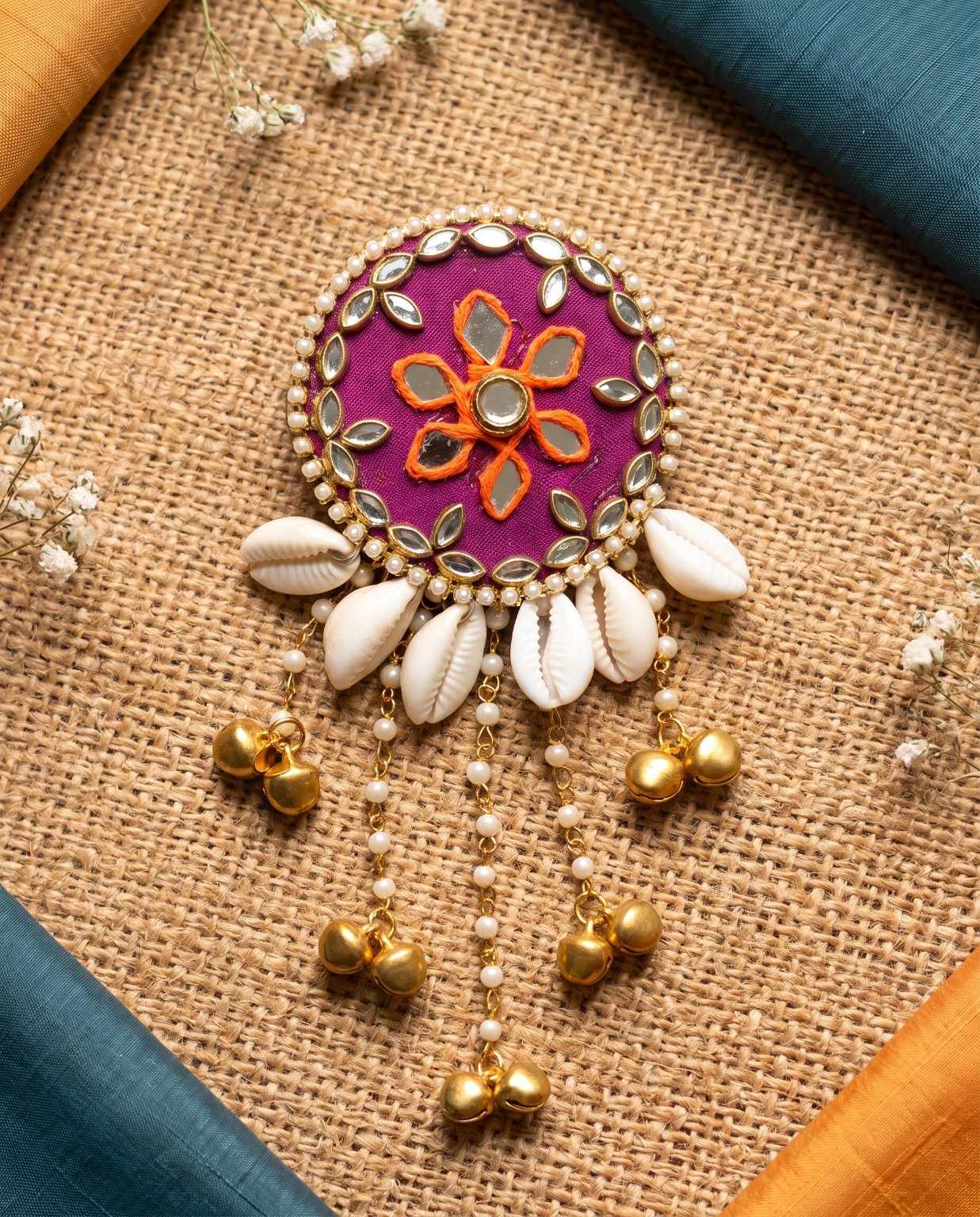 Rangili magenta mirror hair brooch with golden ghungroo and cowrie shells on a jute background