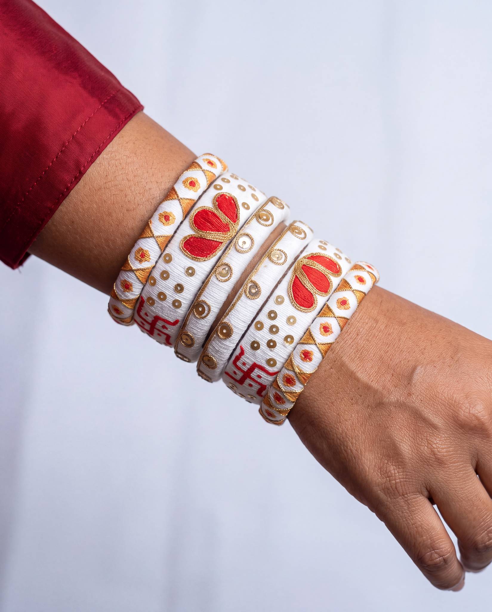Woman wearing white silk thread swastik motif bangles stacked on wrist with red sleeve